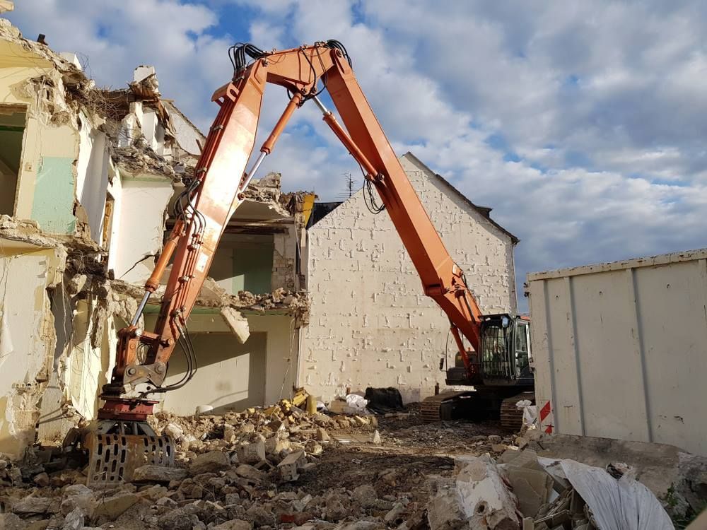 A Large Orange Excavator Is Demolishing A Building — Northern Demolition and Civils in Airlie Beach, QLD