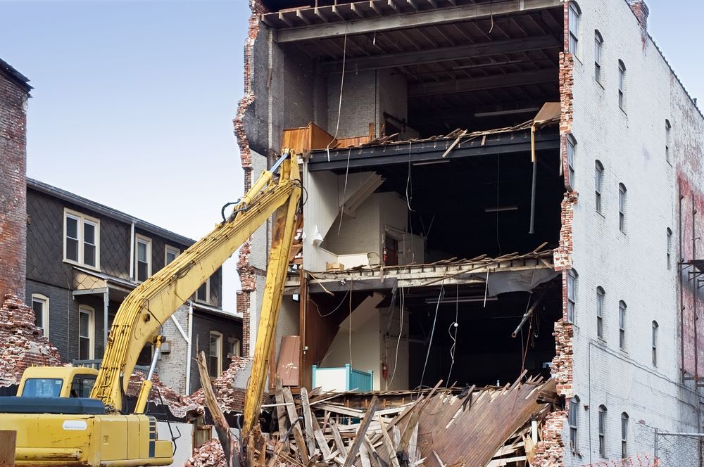 A Large Yellow Excavator Is Demolishing A Building — Northern Demolition and Civils in Proserpine, QLD