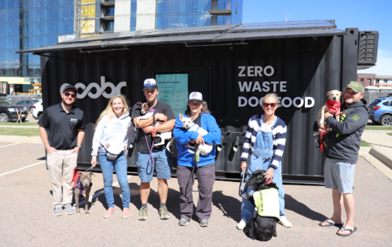 Group of people posing in front of a black “Zero Waste Food” container at an outdoor event.