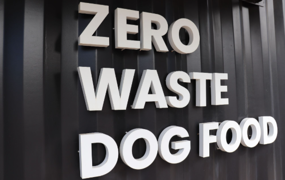 Sign reading “ZERO WASTE DOG FOOD” in bold white letters on a dark corrugated wall