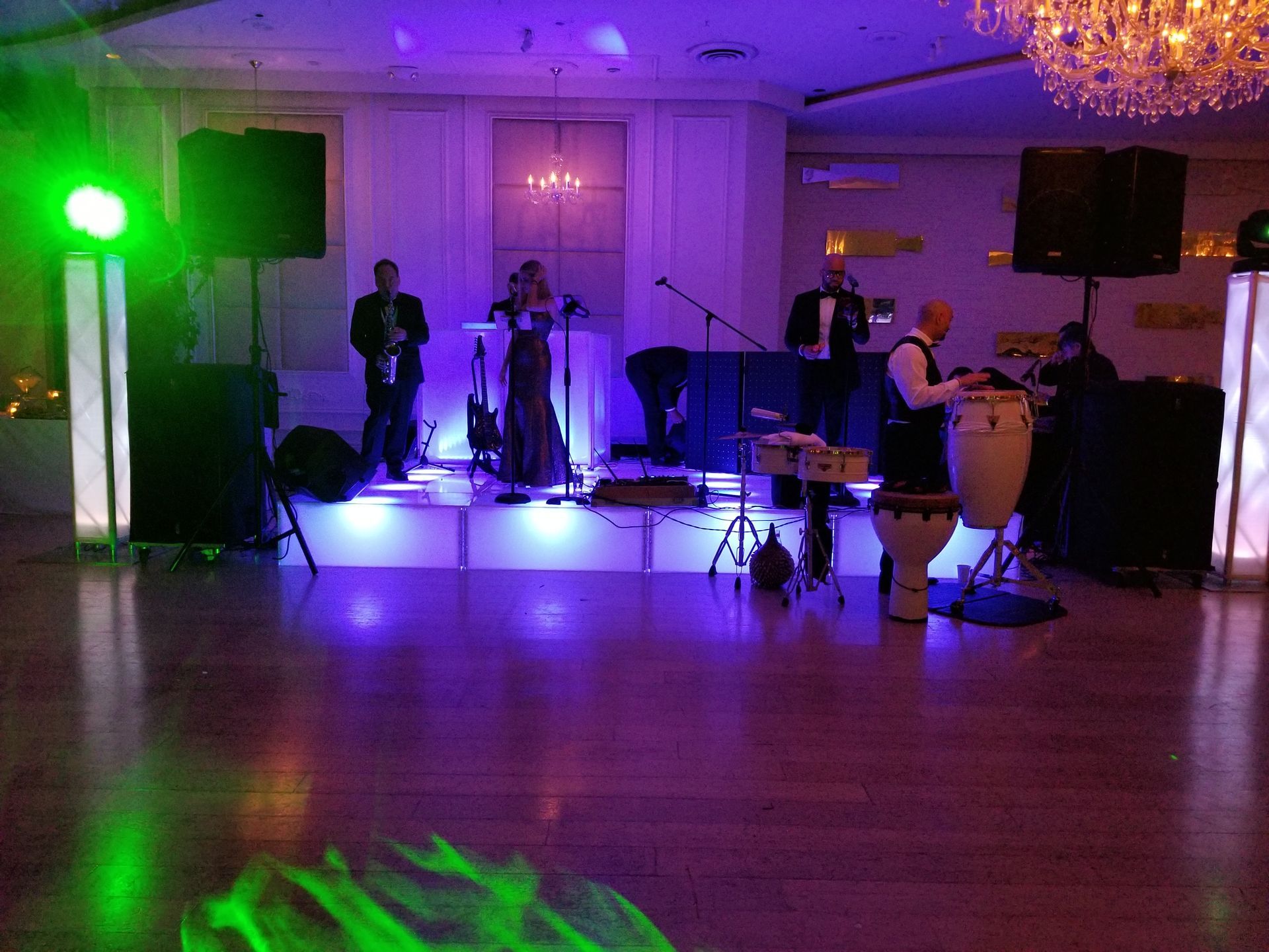 A band performs on a stage lit with purple and green lights in a ballroom.