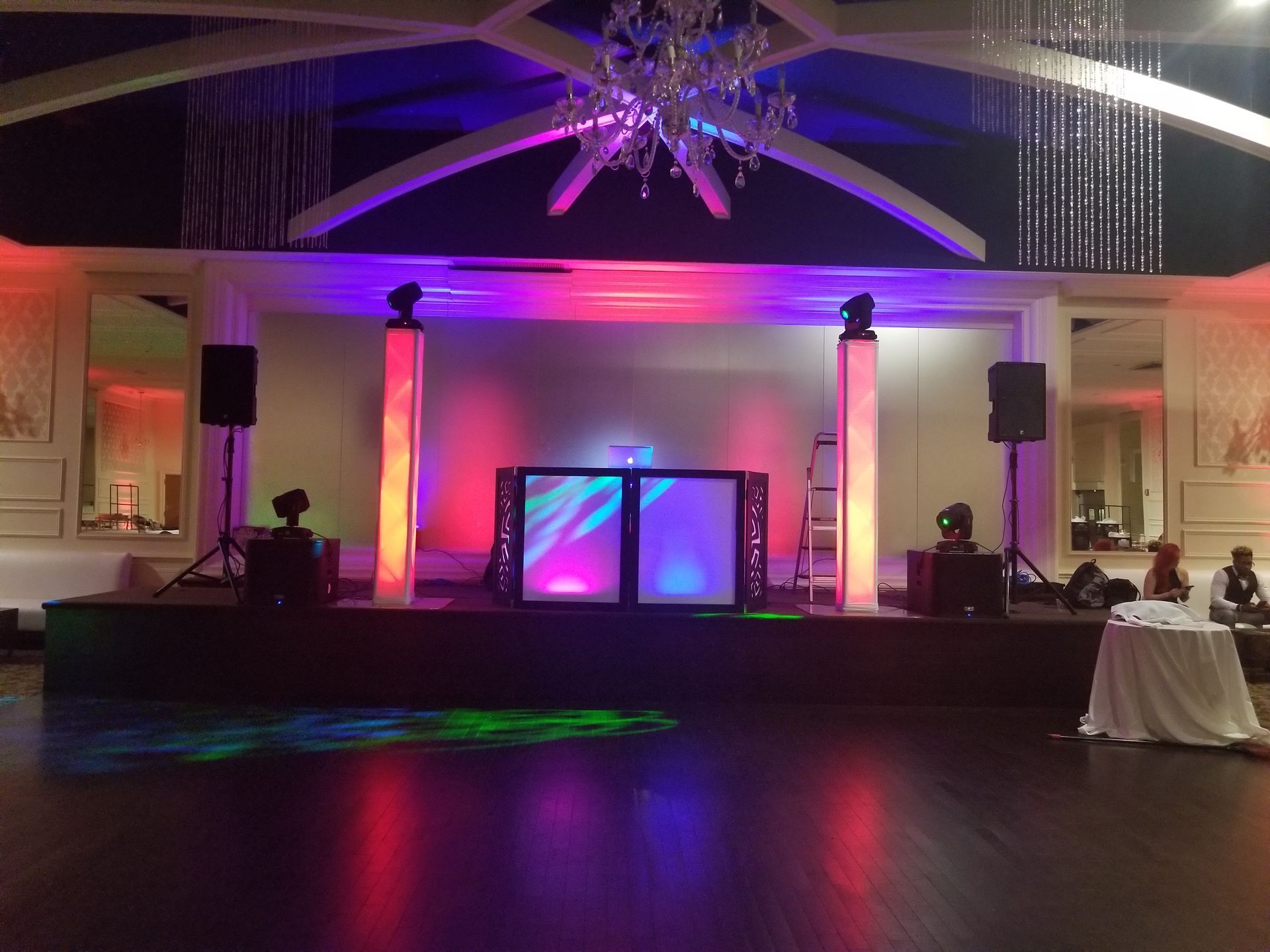 A stage lit with colorful lights, DJ equipment, and speakers set up for an event in a ballroom.