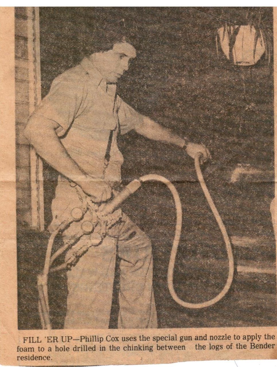 A person uses a hose connected to a gun to inject foam into a hole in the exterior wall of a wooden log home.