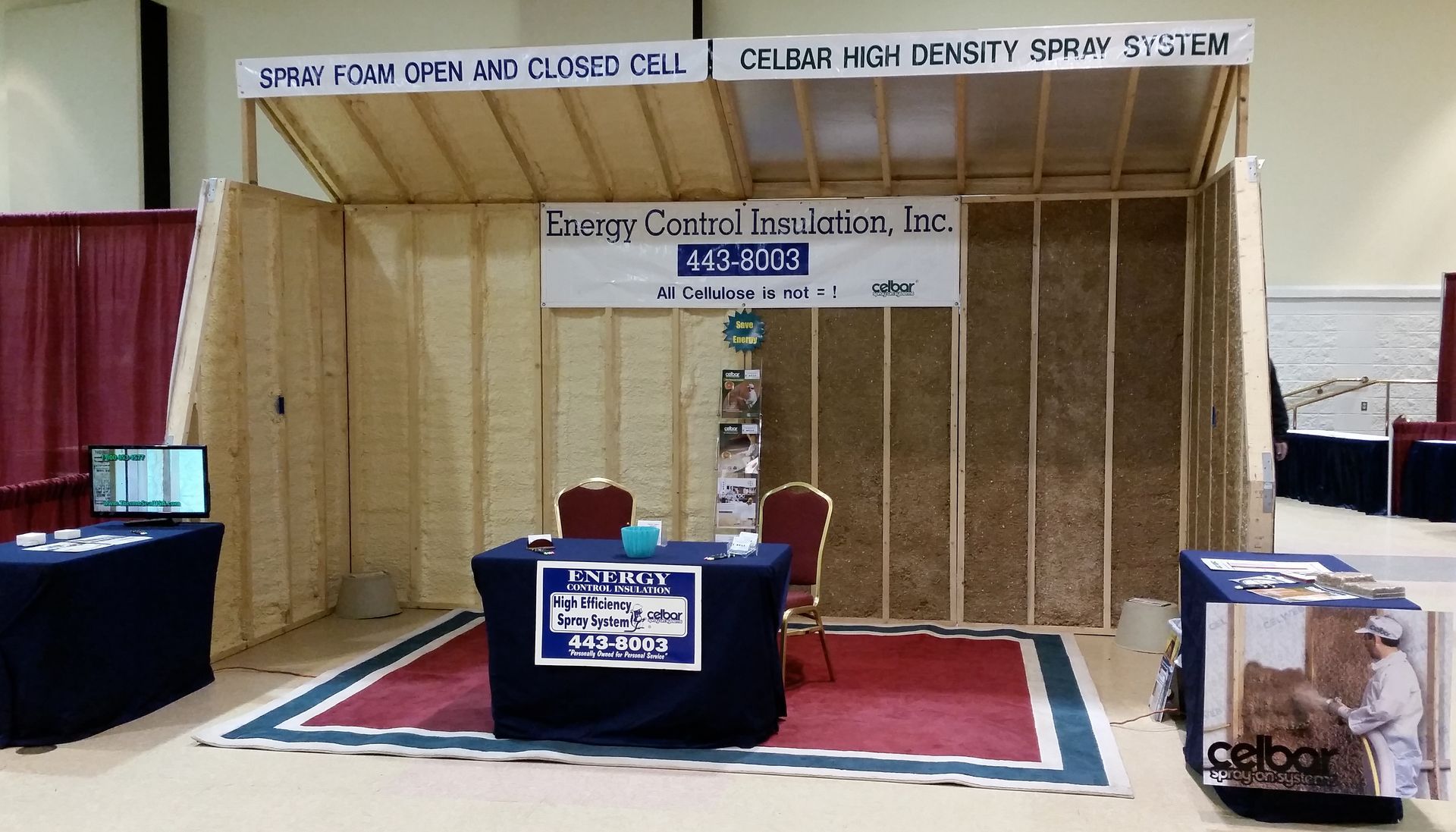 A trade show booth for Energy Control Insulation, Inc. displaying wall insulation types with a table and chairs.