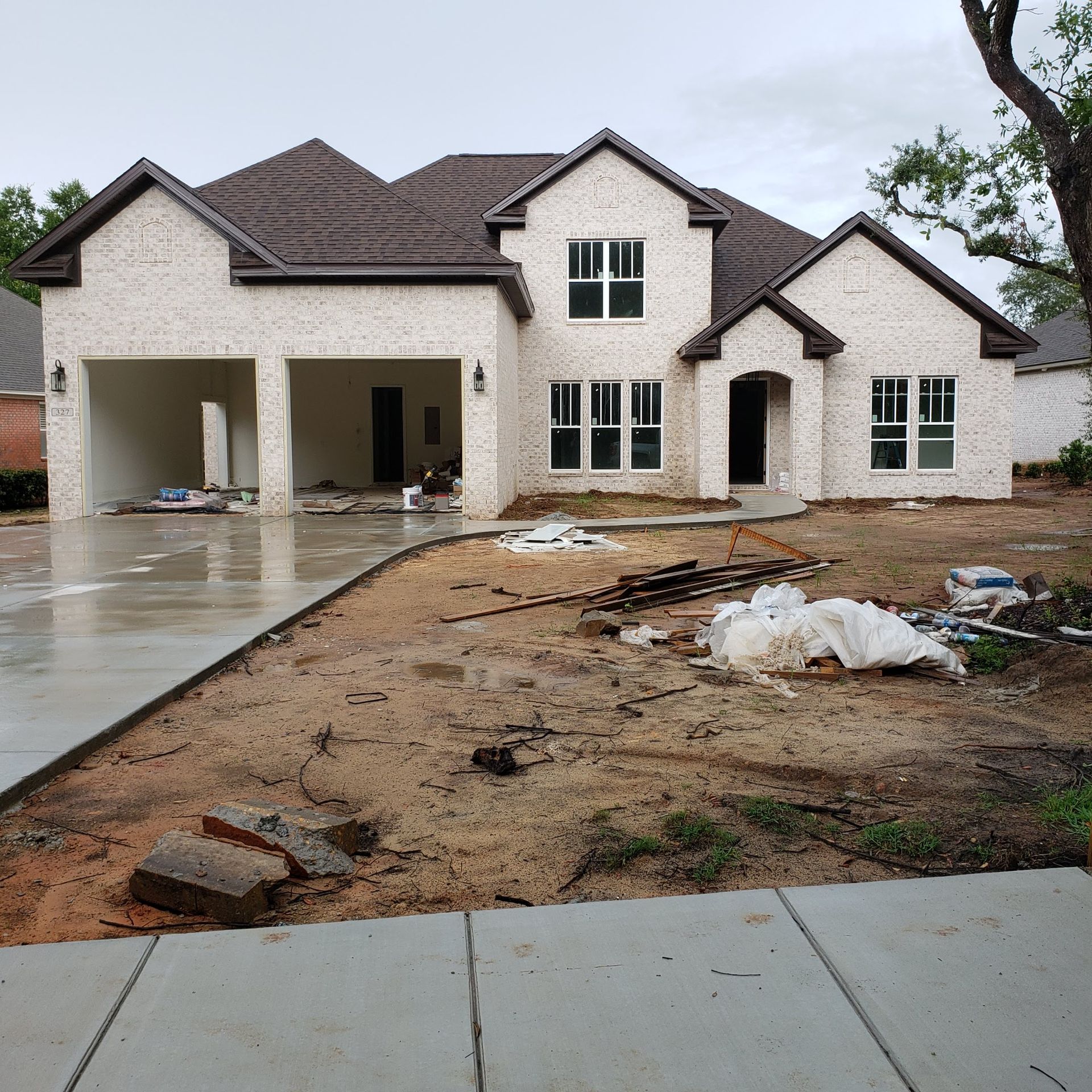 A newly constructed white brick house with a dark brown roof, a concrete driveway, and an unfinished dirt front yard.