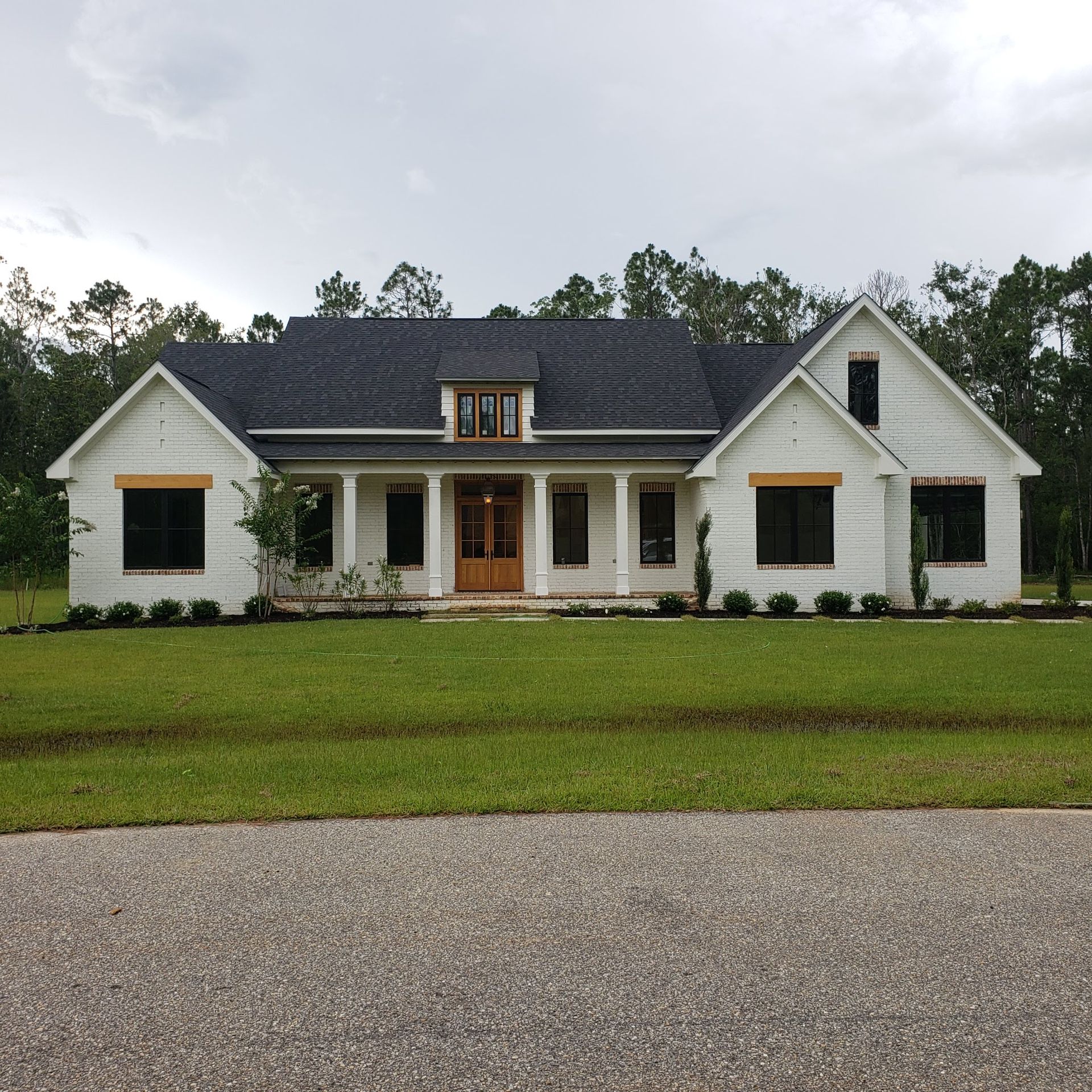 A white, single-story house with a dark gabled roof, a central porch, and a large front lawn, framed by trees.
