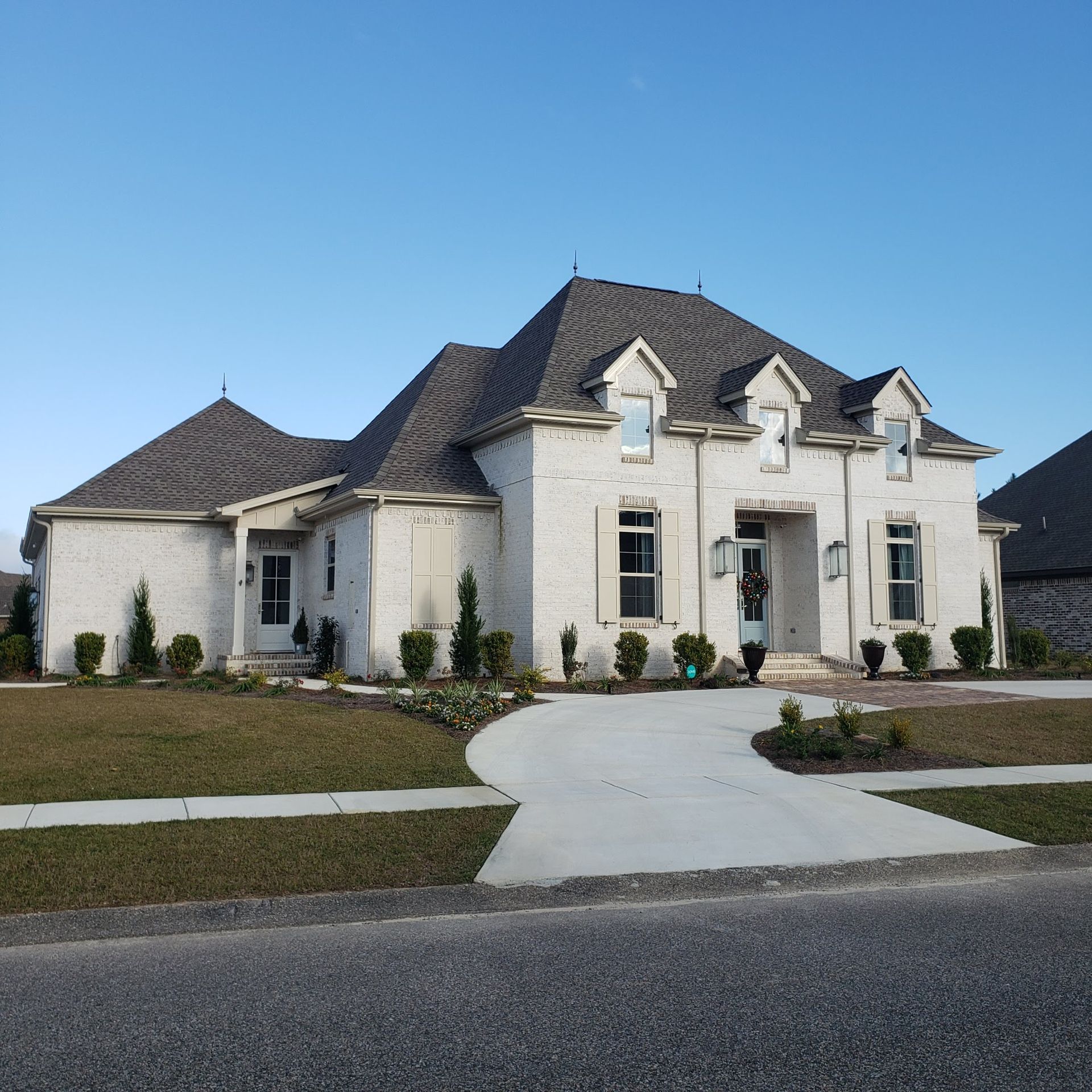A large, single-story light-colored brick house with a dark roof and a concrete driveway under a clear blue sky.