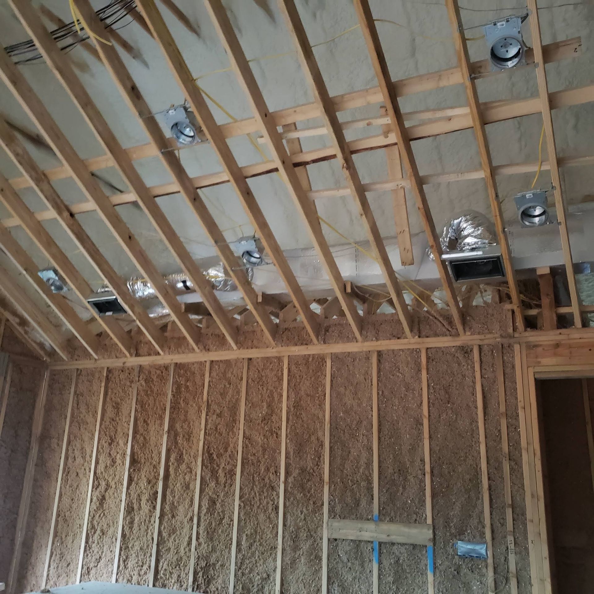 Framed interior wall and ceiling with exposed wooden studs, recessed lighting housings, and flexible ductwork.