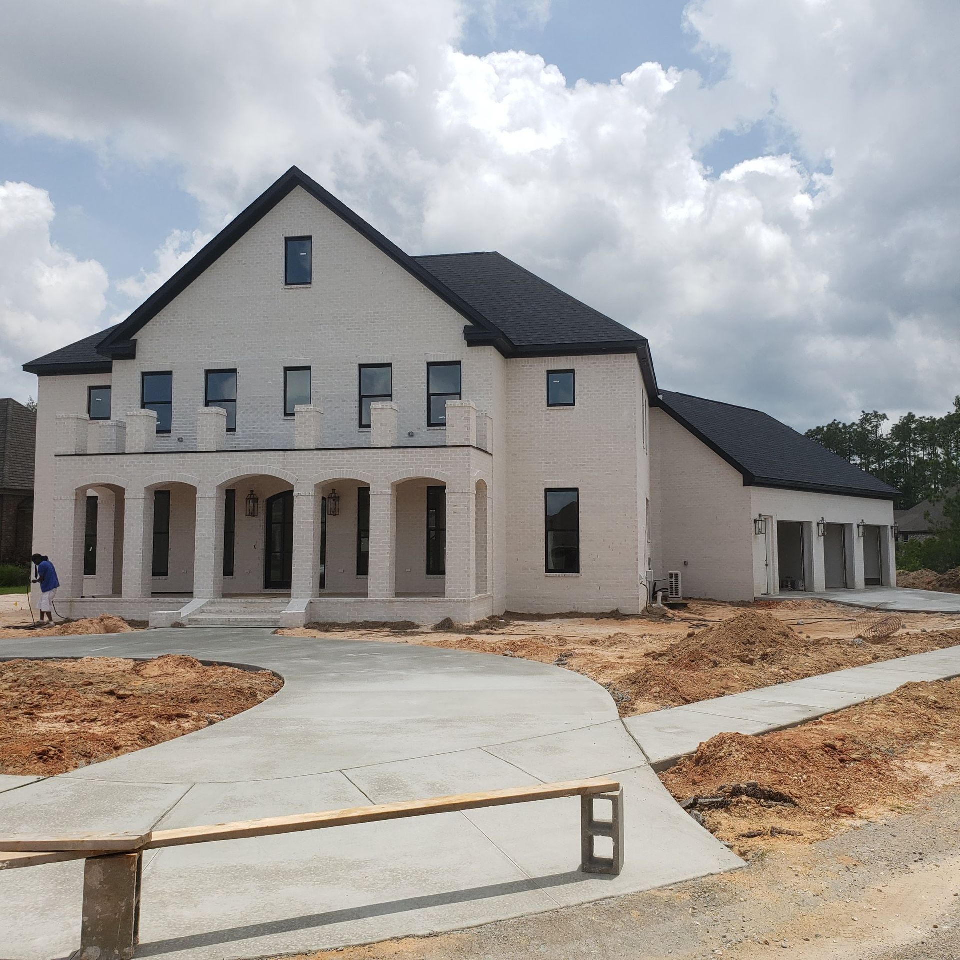 A newly constructed, two-story white brick house with a dark gabled roof and an arched front porch under construction.