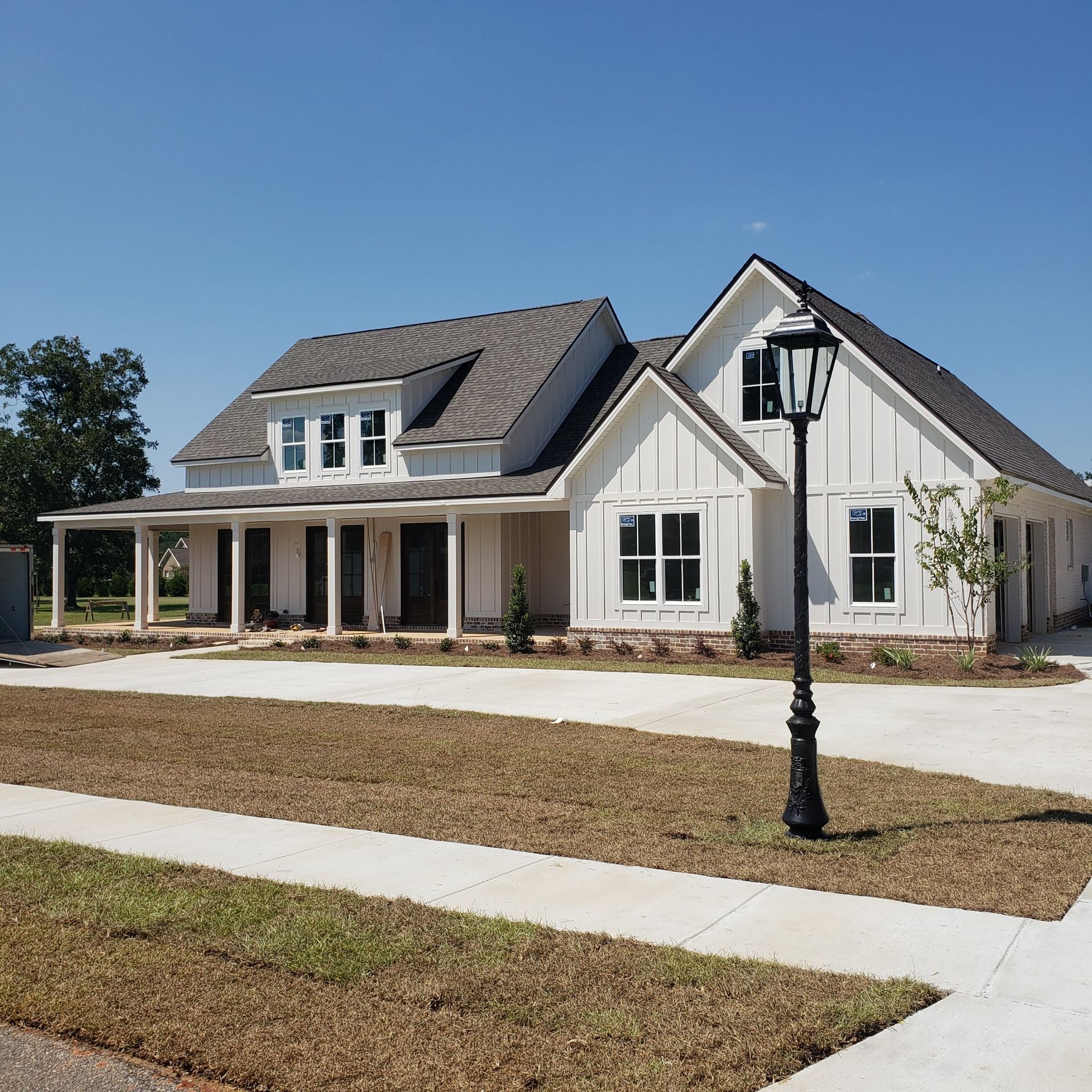 A white farmhouse-style home with board-and-batten siding, a dark roof, and a front porch, viewed from the street.