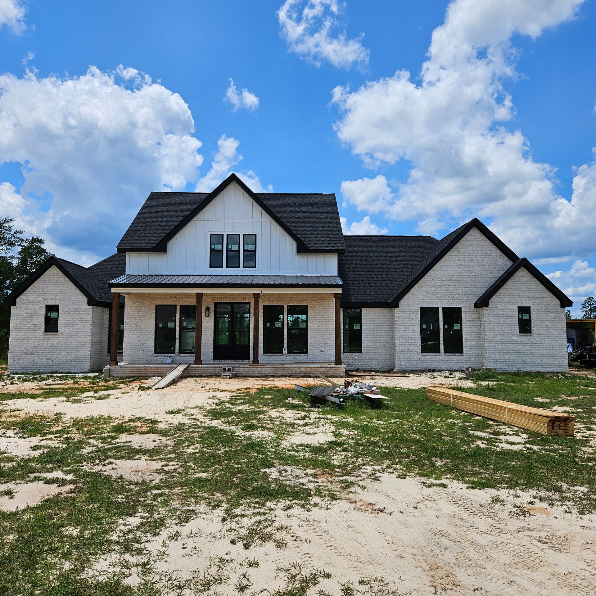 A newly constructed, single-story light stone house with a dark roof and white vertical siding under a blue sky.