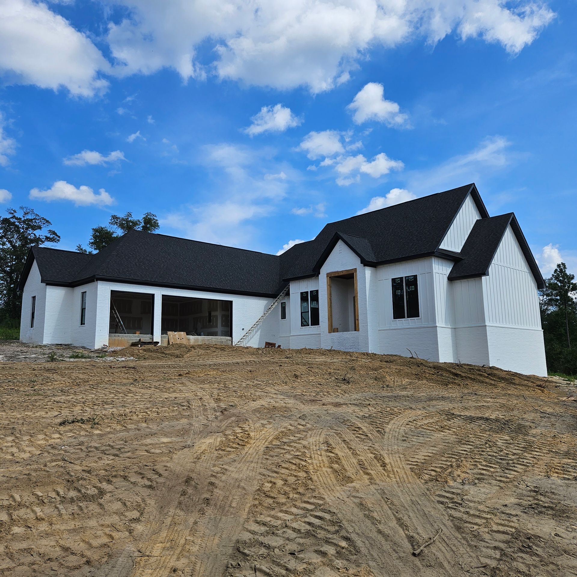 A new single-story house under construction with white exterior walls and a black roof against a bright blue sky.