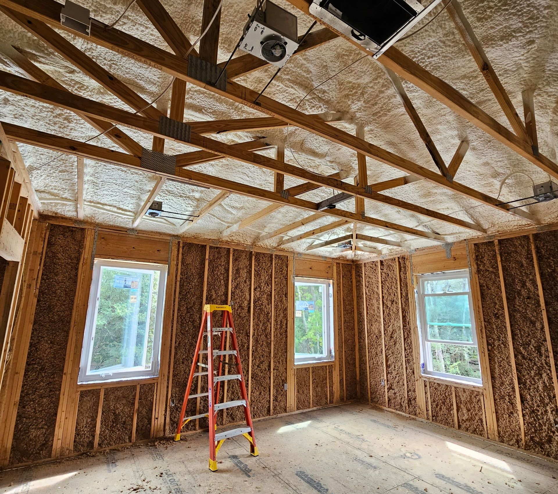An interior view of a room under construction with exposed wooden wall studs, insulation, and roof trusses.