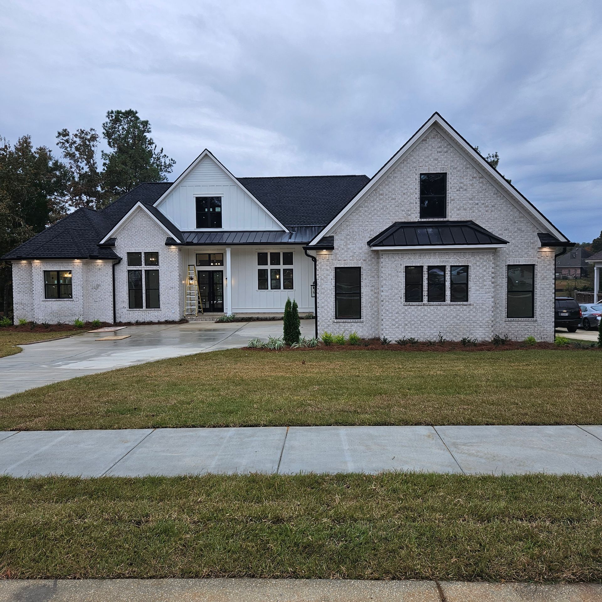 A modern, white-brick house with black roof accents, large windows, and vertical siding, set behind a front lawn.