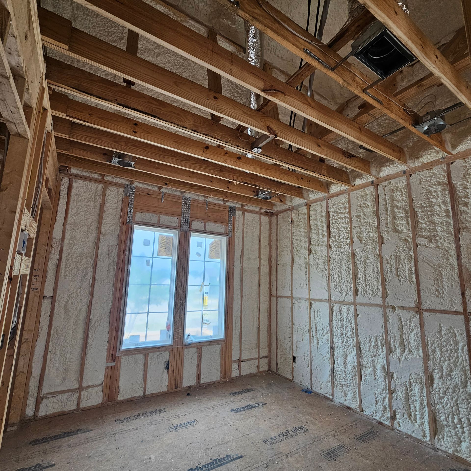 An unfinished room under construction, showing spray foam insulation on the walls and exposed ceiling joists.