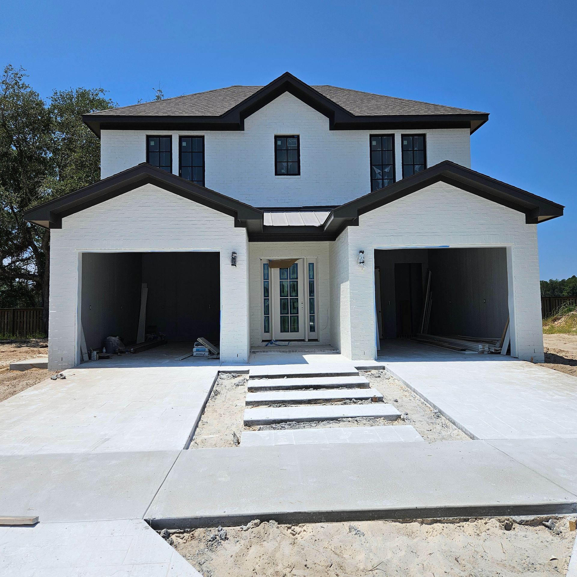 A two-story, white-brick suburban house with a two-car garage, a central entrance, and a new concrete driveway.