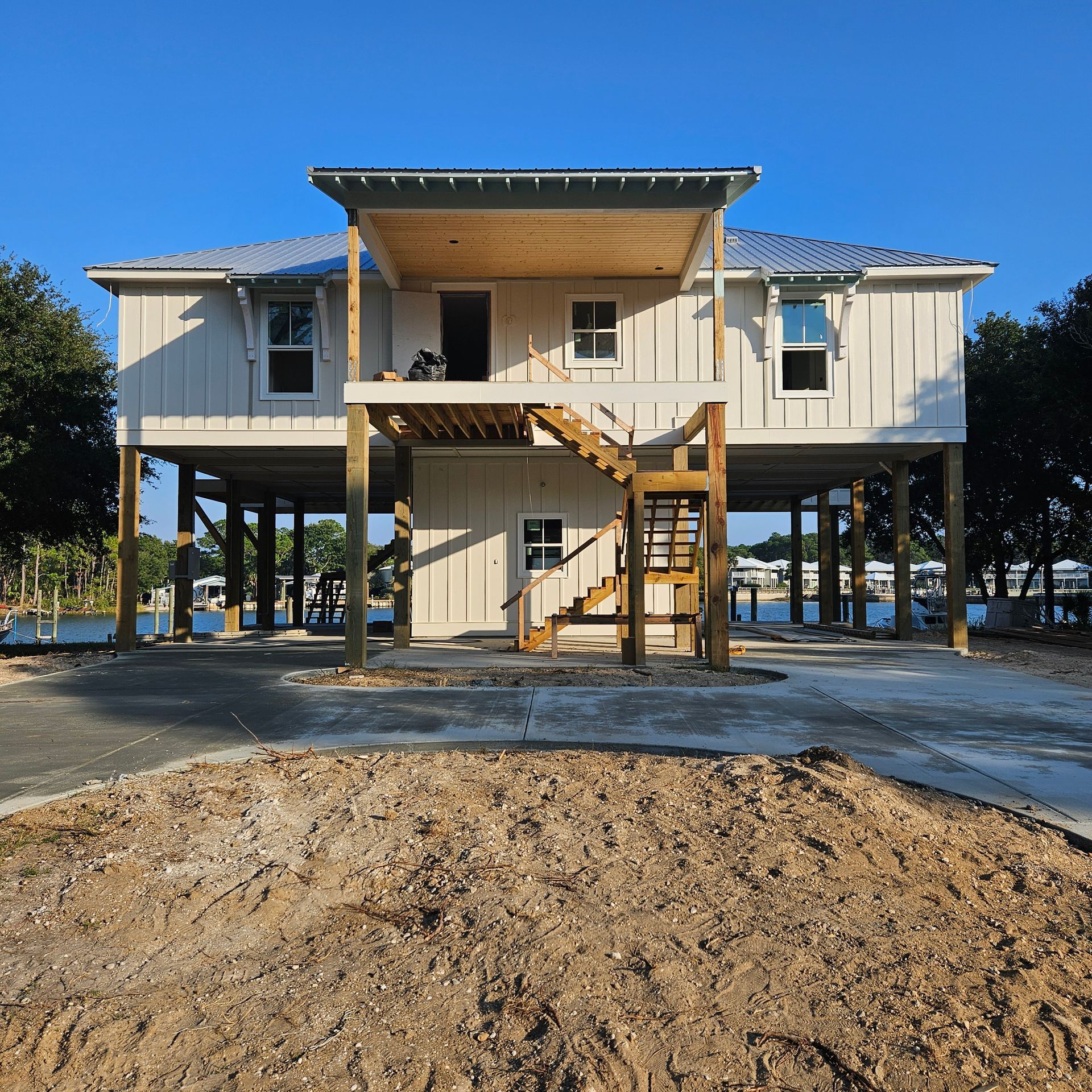 A white, elevated stilt house with a wooden porch and central staircase, set against a clear blue sky.