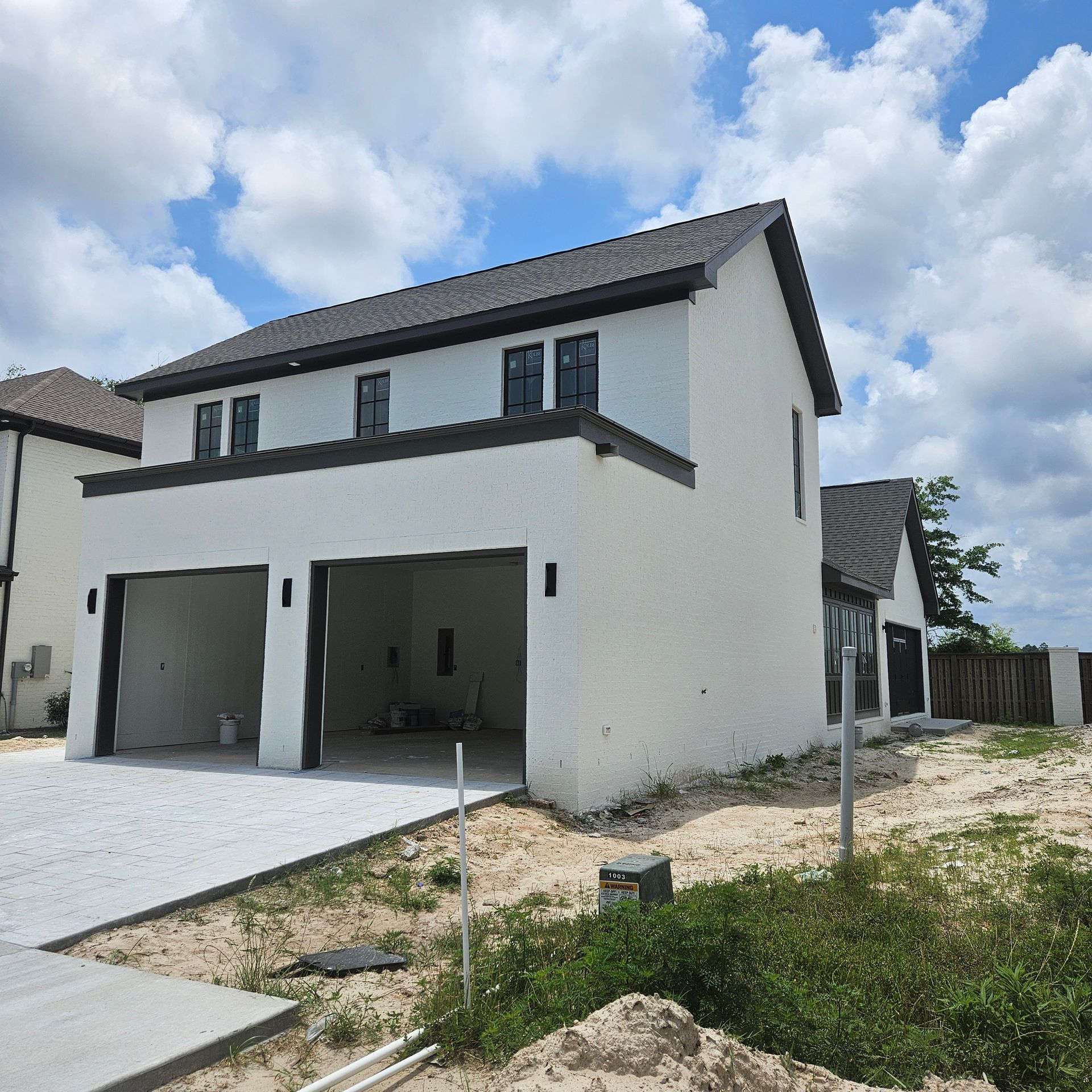 A two-story, white stucco house under construction with a two-car garage, dark trim, and a shingled roof.