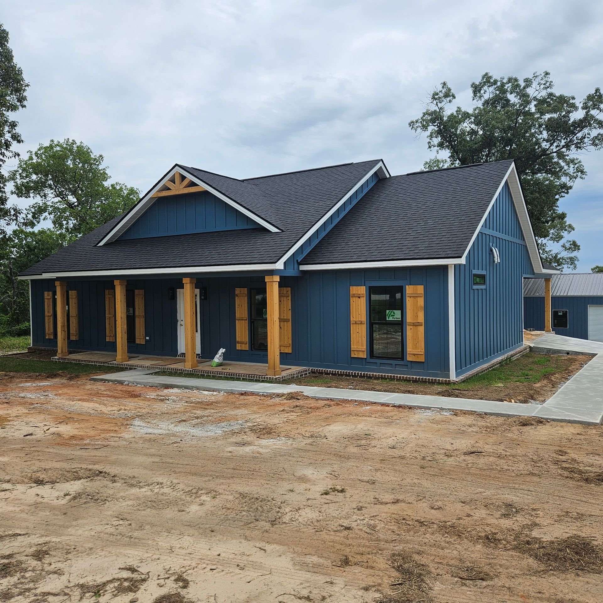 A blue house with board and batten siding, dark roof, and wooden porch columns under a cloudy sky.