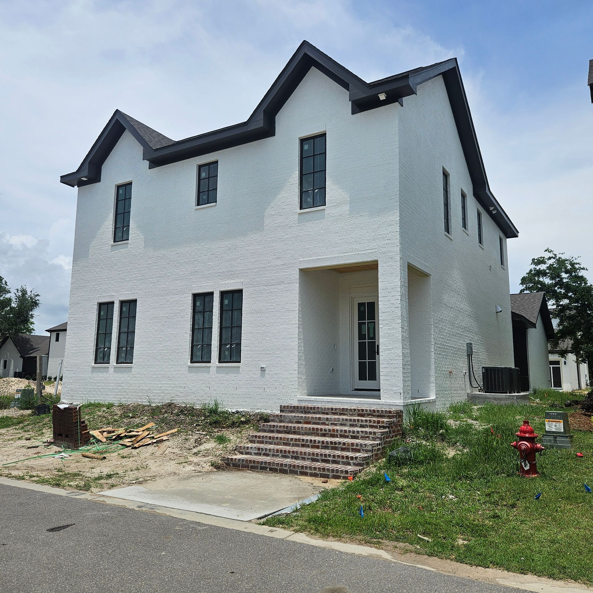 A two-story, white, textured-brick house with a steep gabled roof and dark window frames under a partly cloudy sky.