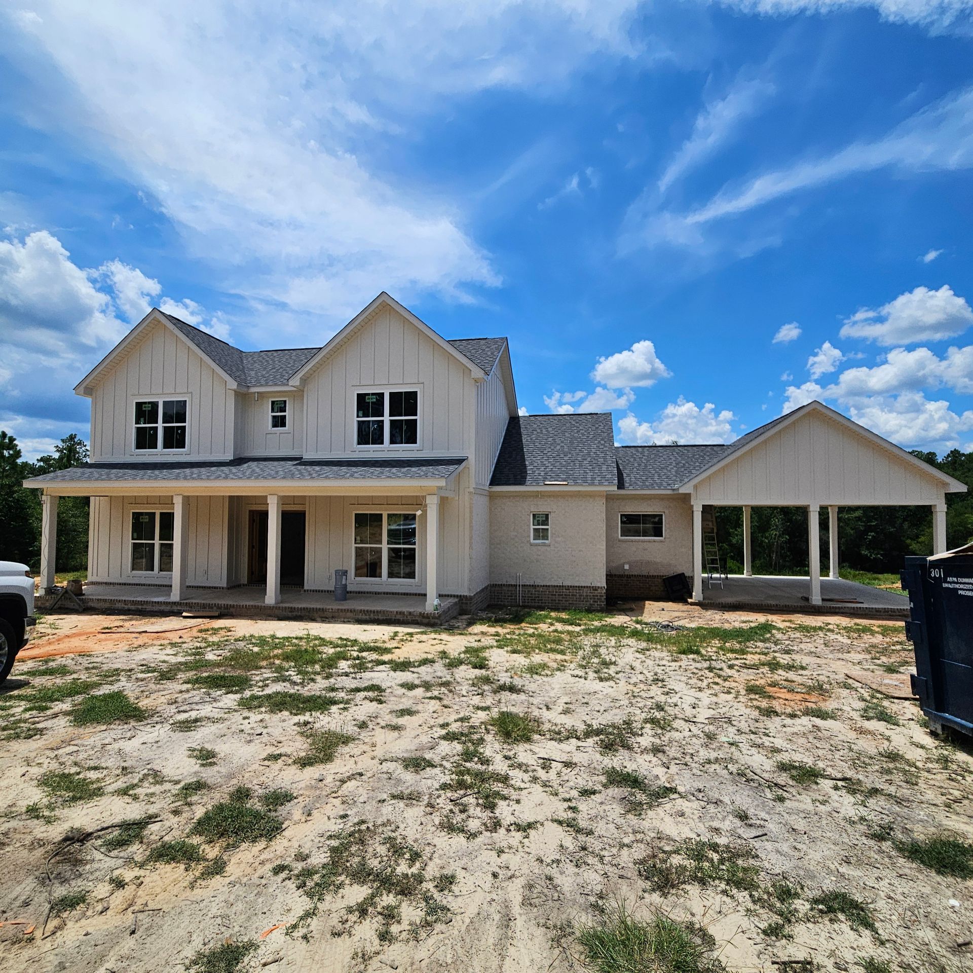 A newly built two-story house with white vertical siding, a front porch, and an attached carport under a blue sky.