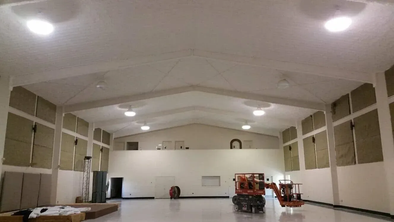 A large, high-ceilinged room with white walls and a light floor, currently undergoing construction or renovations.