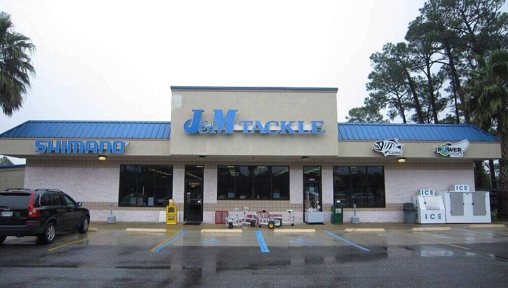 A J&M Tackle shop storefront with a blue roof, glass windows, and a car parked in front on an overcast day.