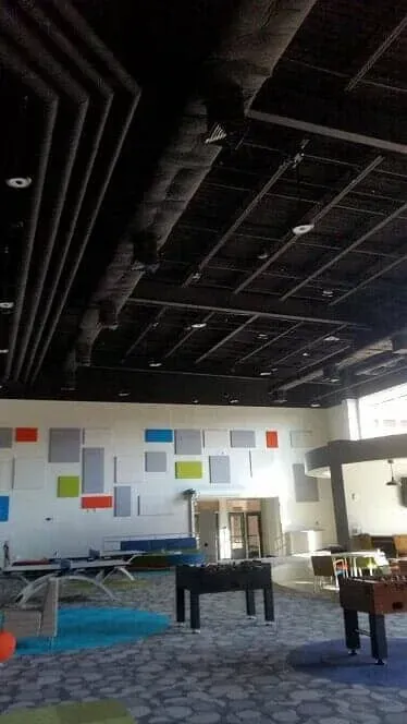 A modern recreational room with foosball tables, lounge seating, and geometric colorful panels on a white wall.