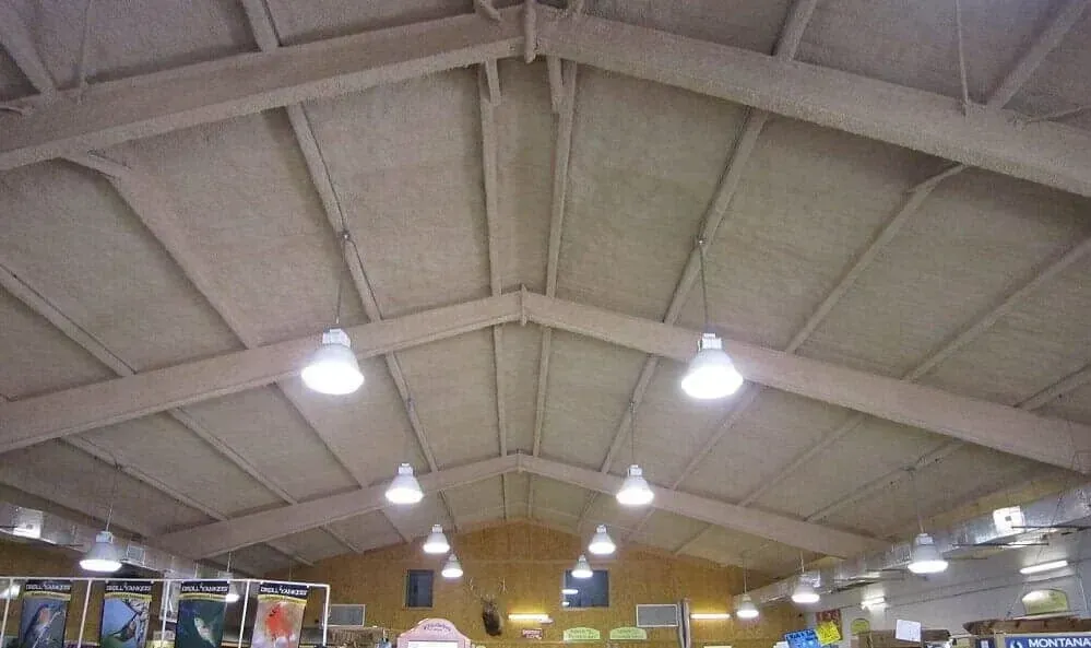 A view looking up at the high, slanted ceiling and exposed wooden beams of a large store interior with hanging lights.