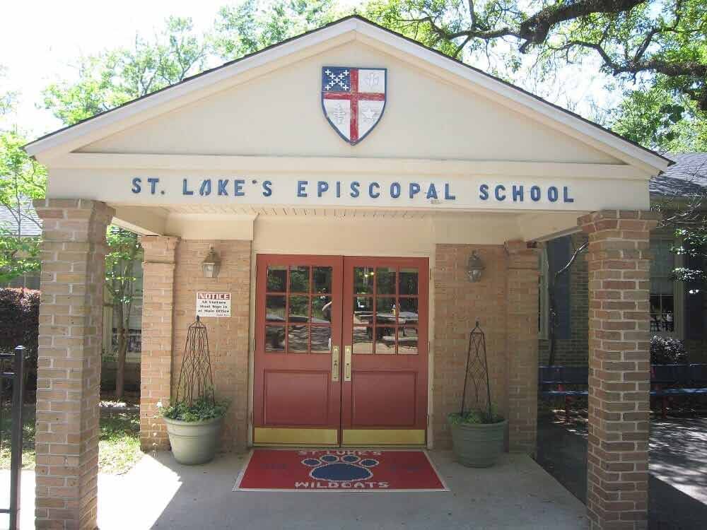 The entrance to St. Luke's Episcopal School with red double doors, brick pillars, and a school crest on the gable.