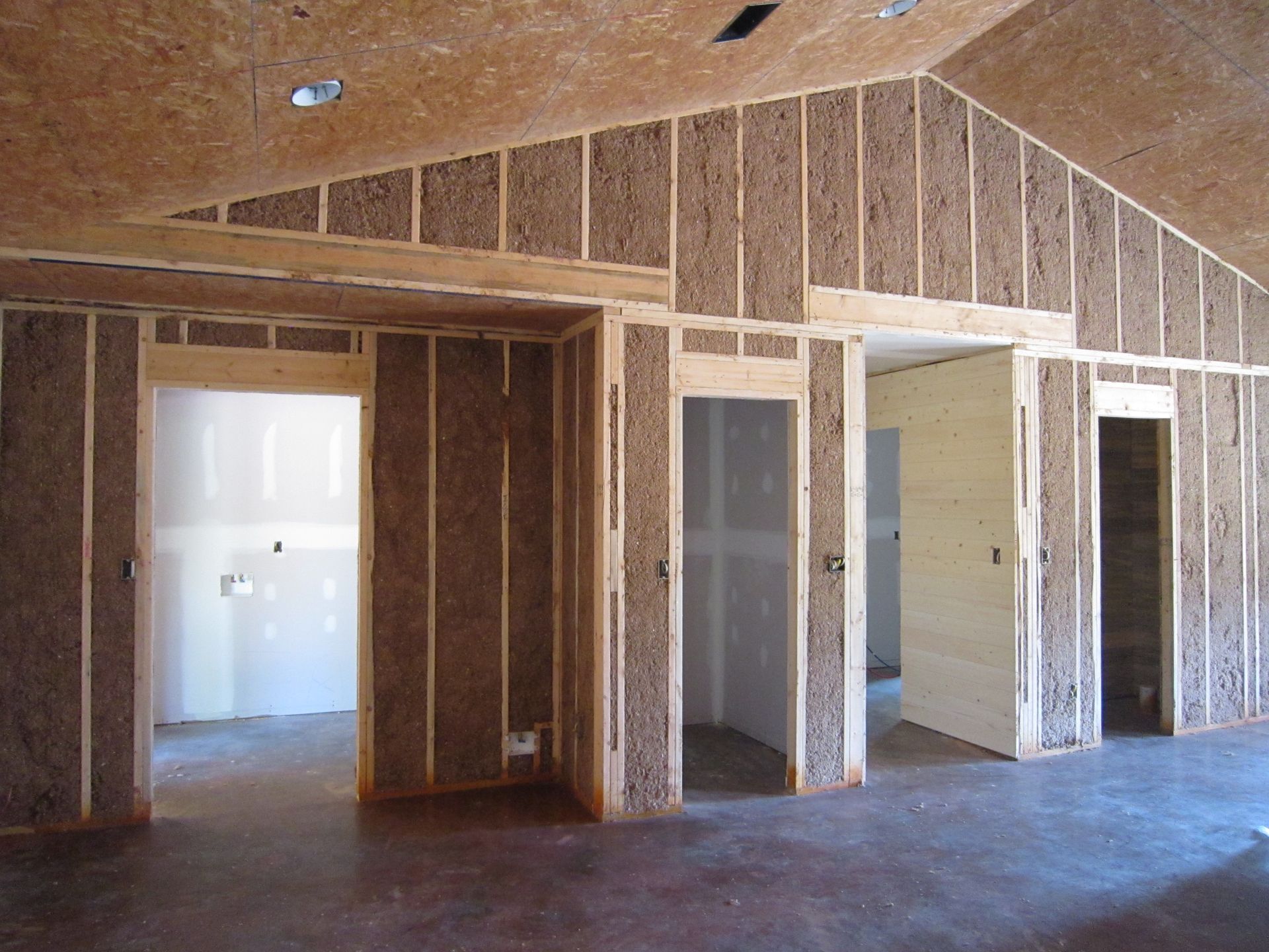Construction site interior showing unfinished stud walls with cellulose insulation and exposed OSB ceiling.
