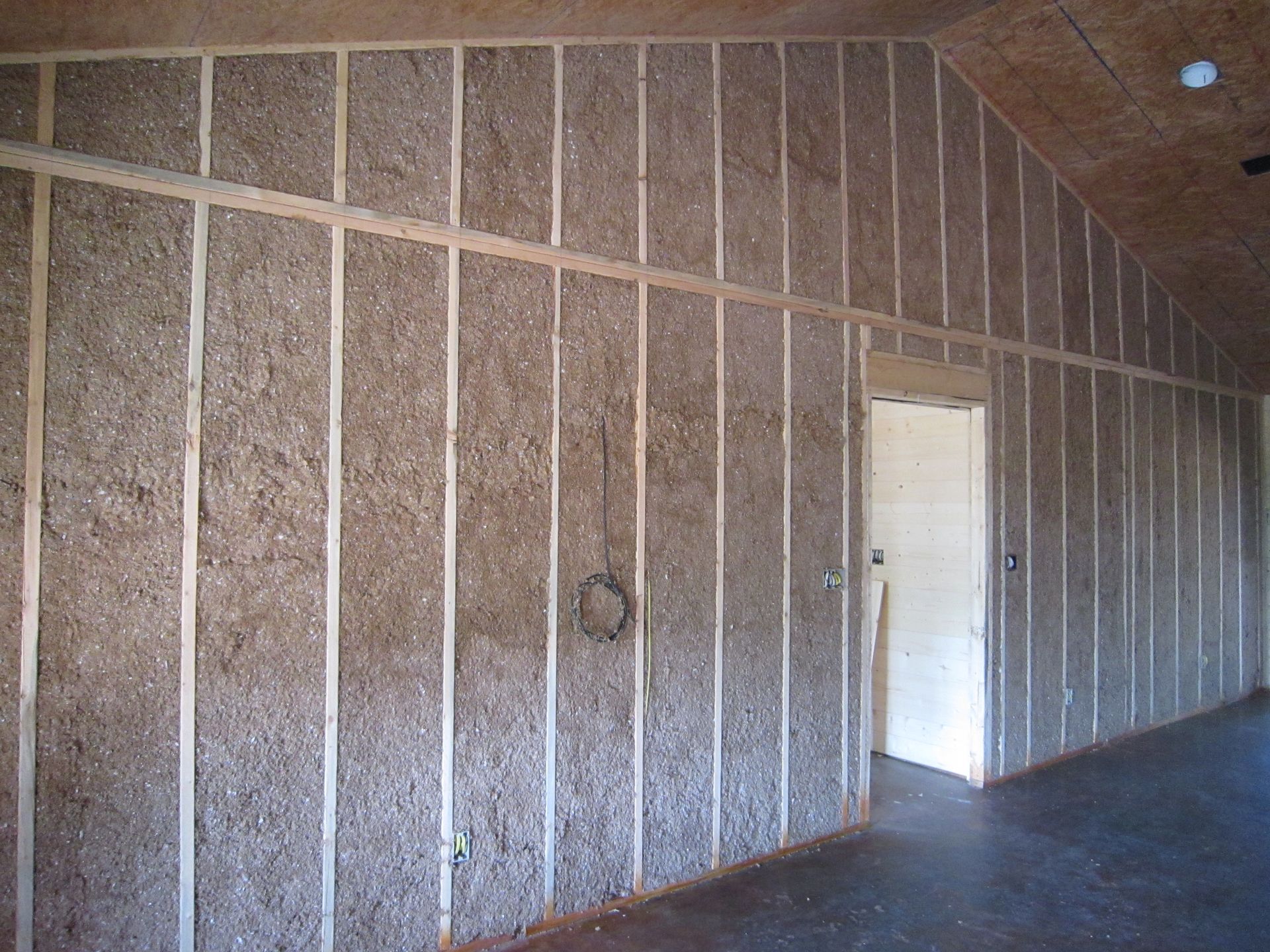 Interior wall under construction with wood studs and straw-bale or hemp-crete insulation panels.