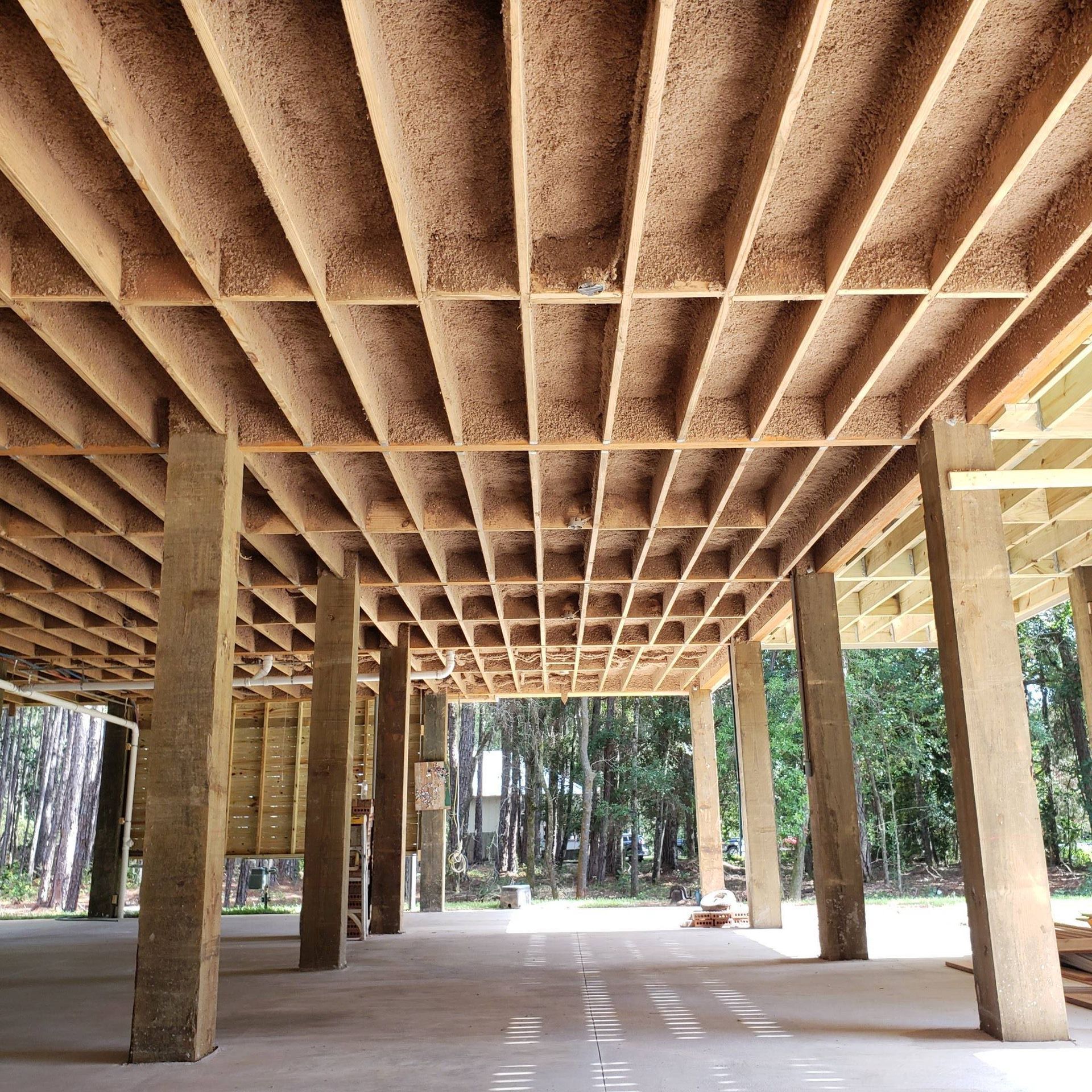 View from below of a wooden floor structure supported by several concrete pillars over a concrete foundation.