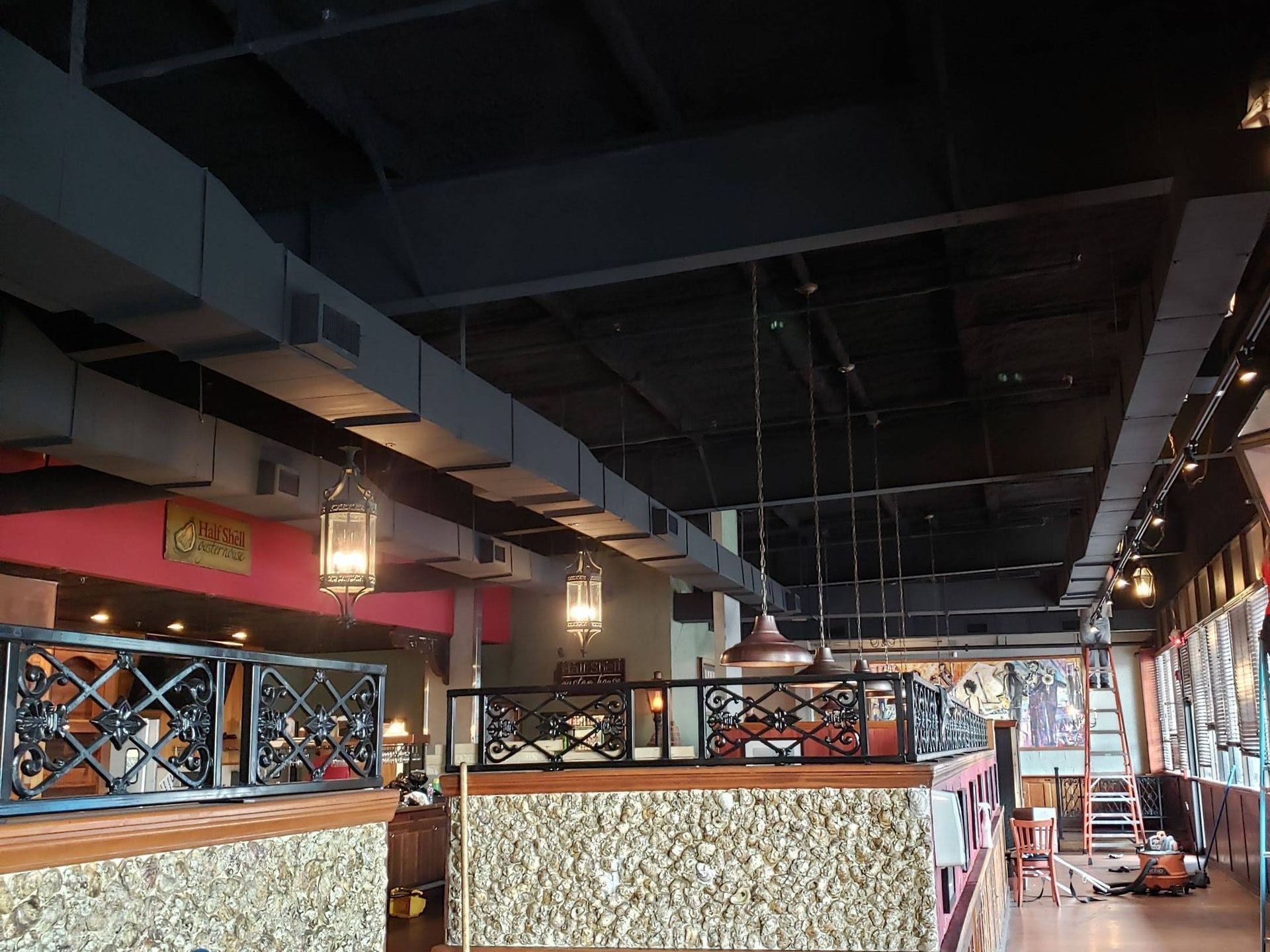 An interior shot of a restaurant with dark, exposed ceiling rafters, hanging lantern-style lights, and stone-tiled walls.