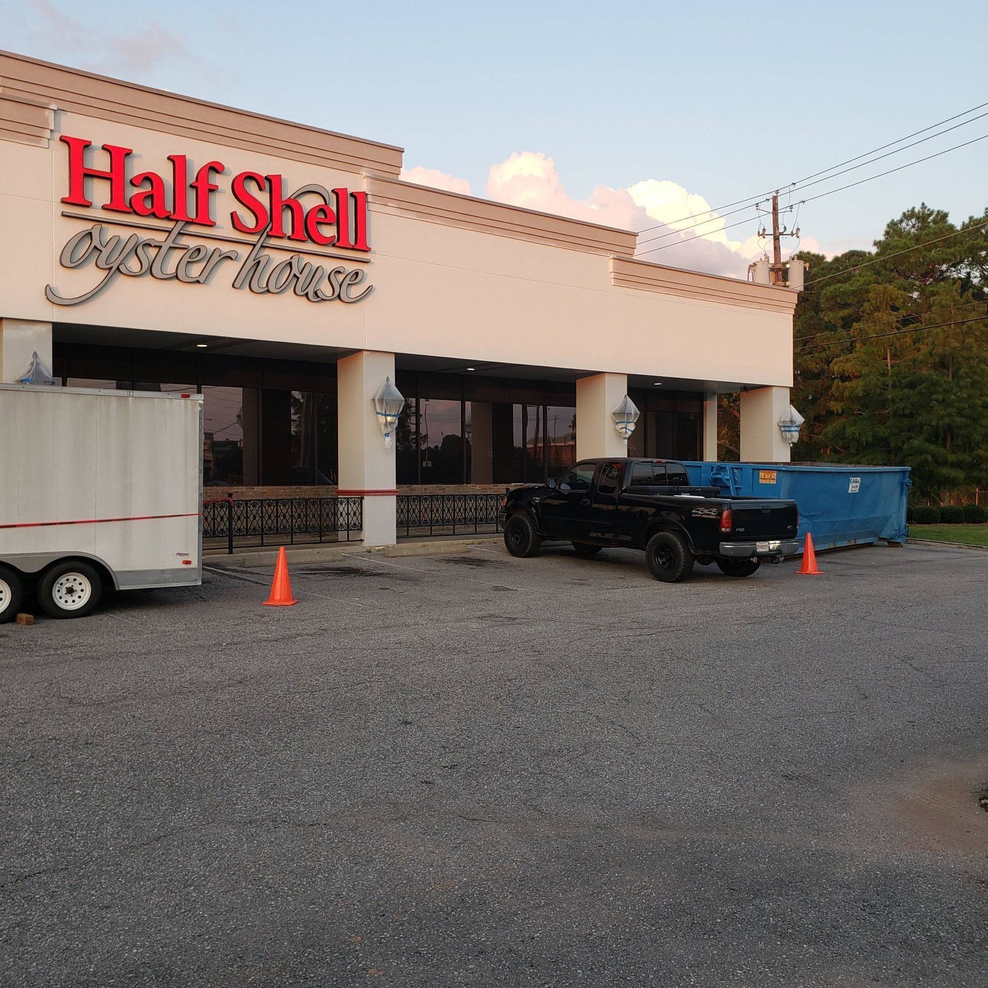 Half Shell Oyster House restaurant exterior featuring a white building, parked truck, trailer, and a blue dumpster.