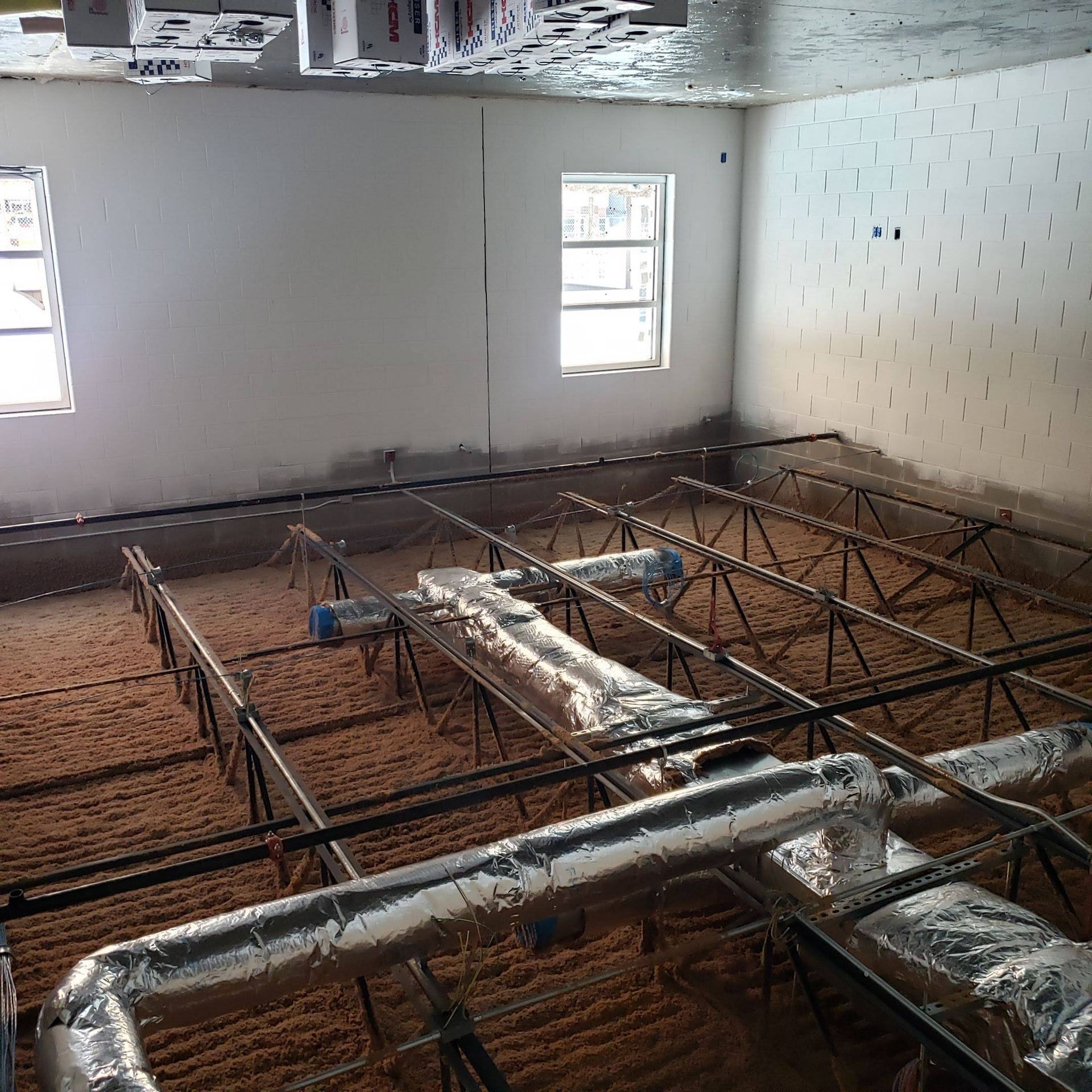 Unfinished construction interior with metal framing, ductwork on brown insulation, and two windows on a white wall.