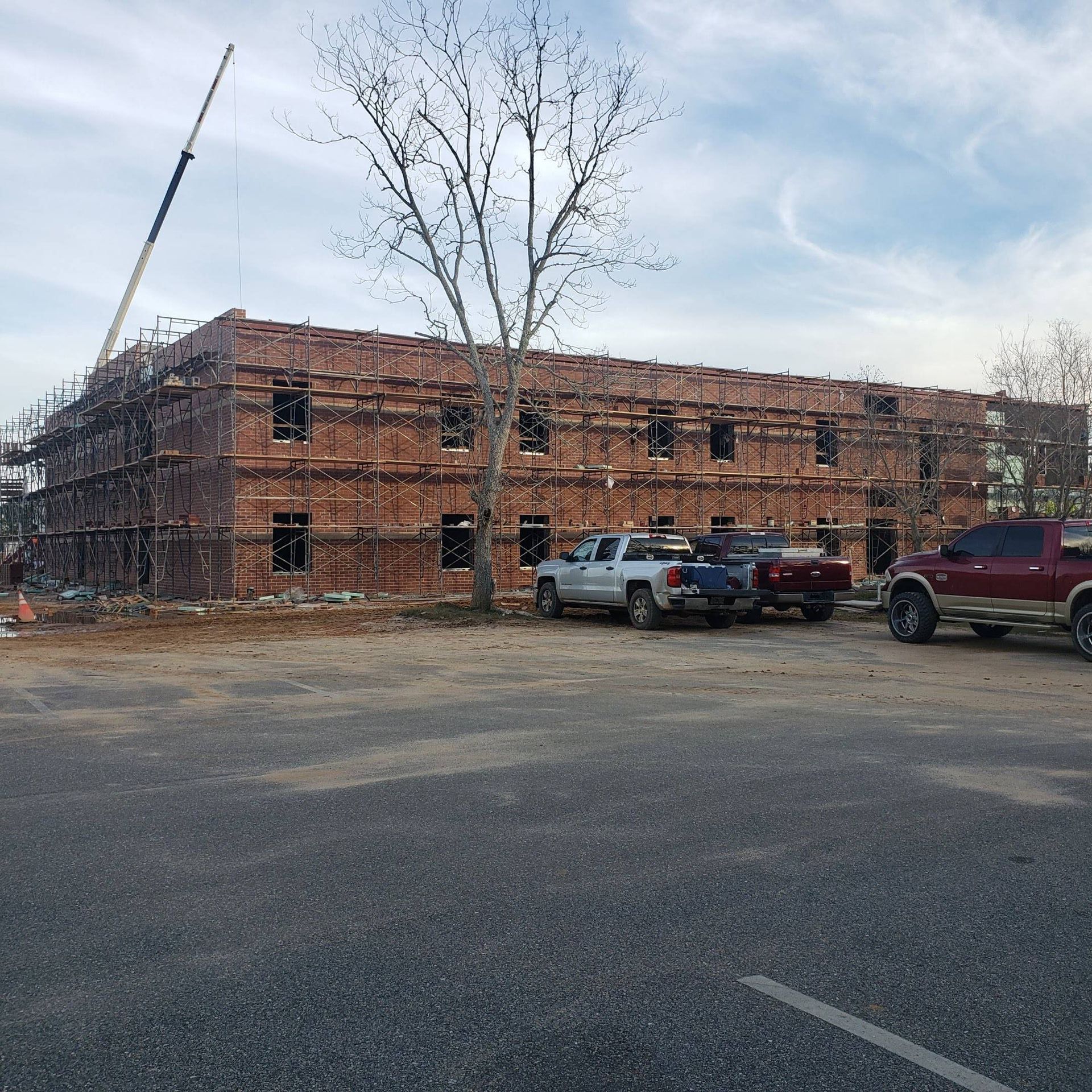 A three-story brick building under construction with scaffolding, surrounded by trucks in a parking lot.