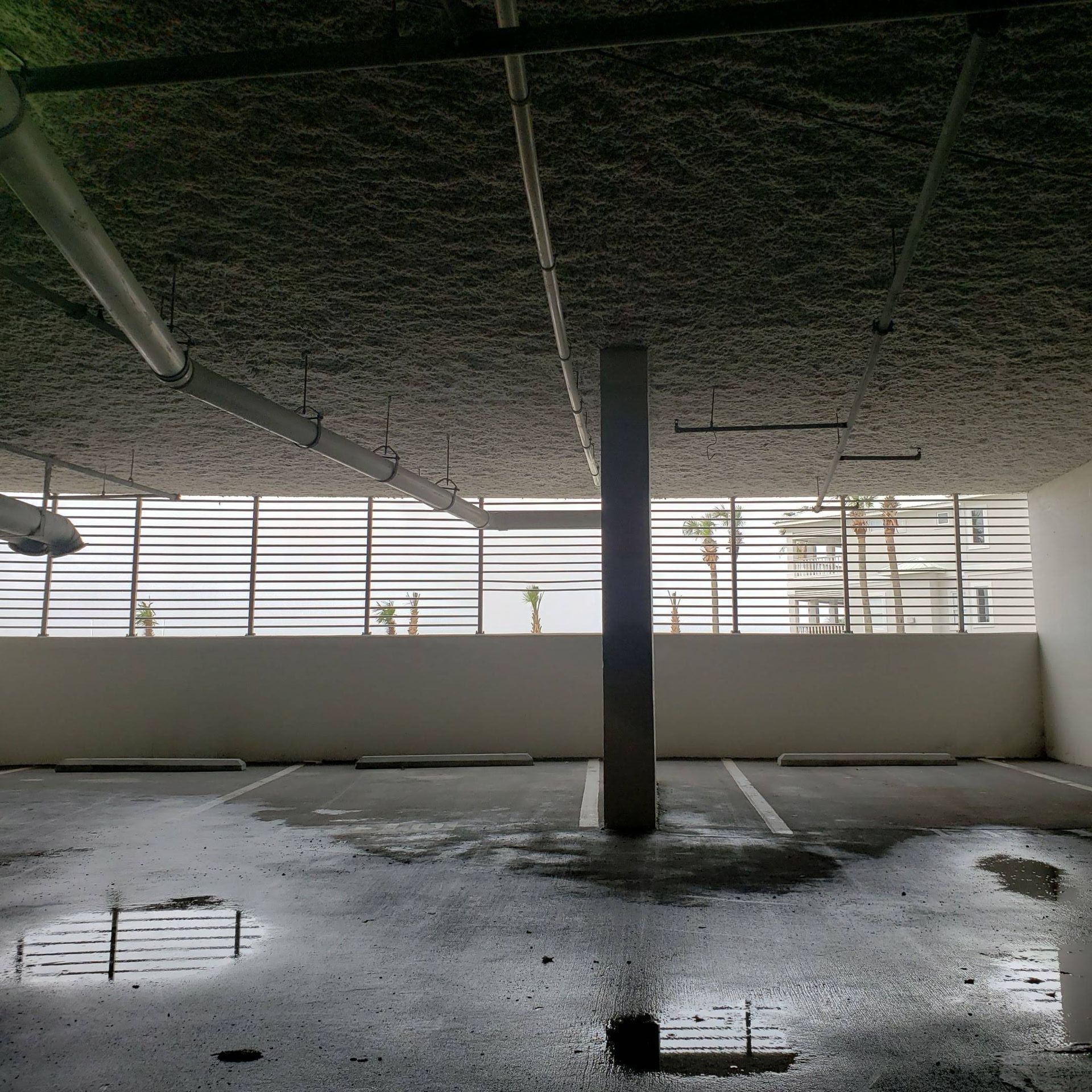 An empty parking garage level with a central support pillar and wet concrete floor showing reflections of the ceiling.