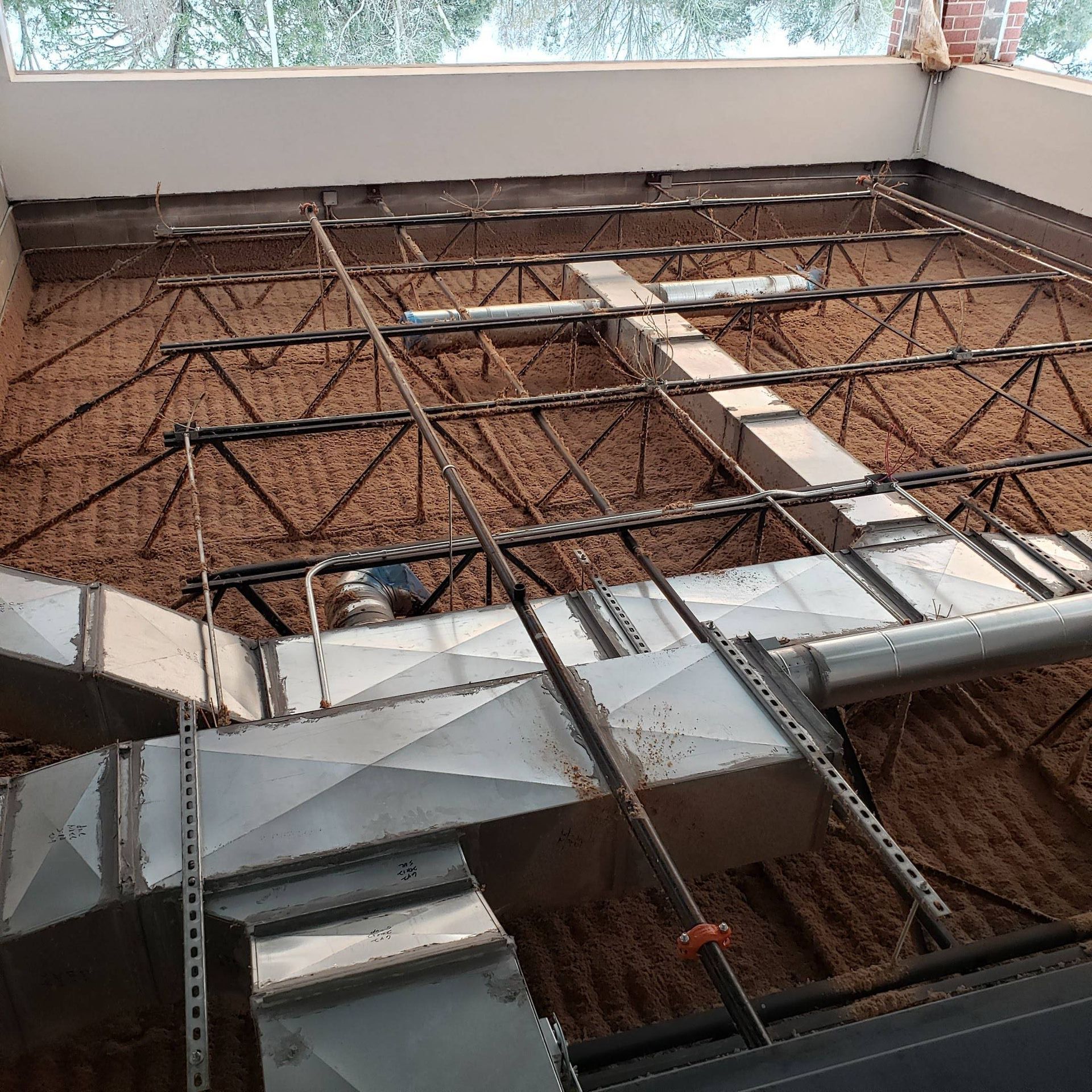HVAC metal ductwork installed above a suspended ceiling grid and open-web steel joists in an unfinished interior space.