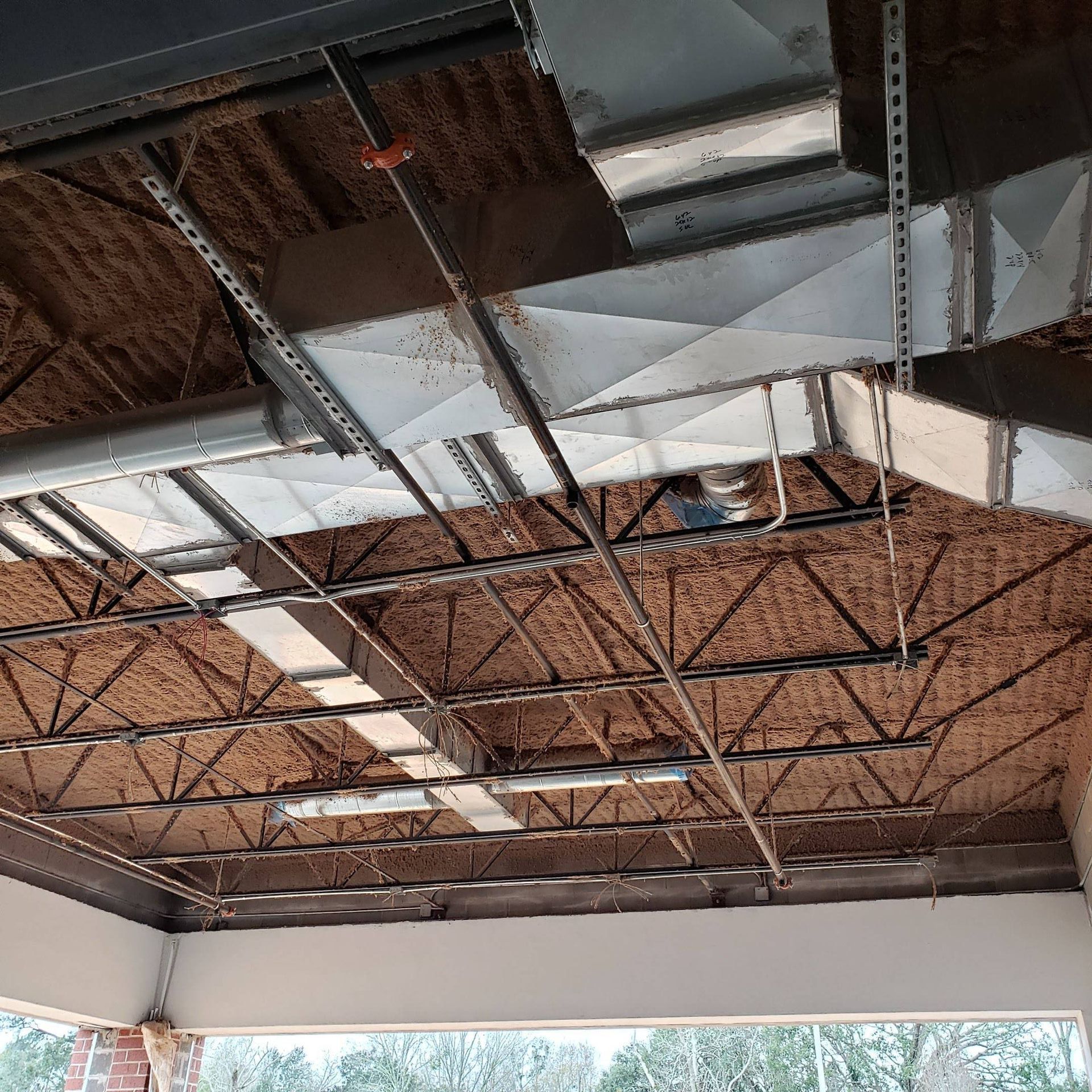 Exposed ceiling structure featuring metal support beams, HVAC ductwork, and electrical conduits in an unfinished space.