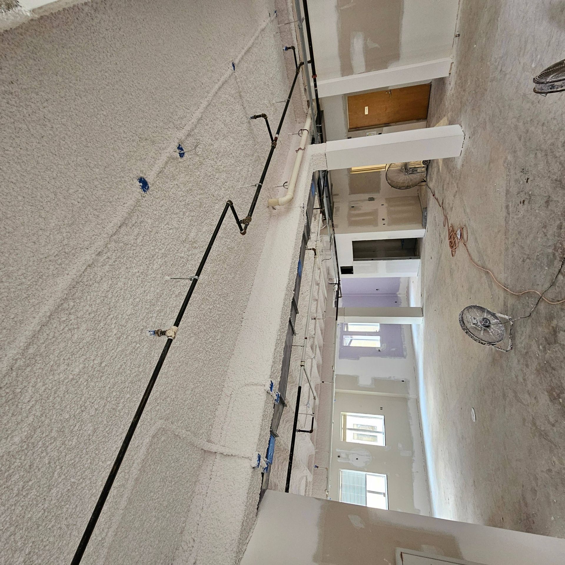Construction site interior featuring exposed concrete ceilings, black electrical conduits, and unfinished drywall walls.