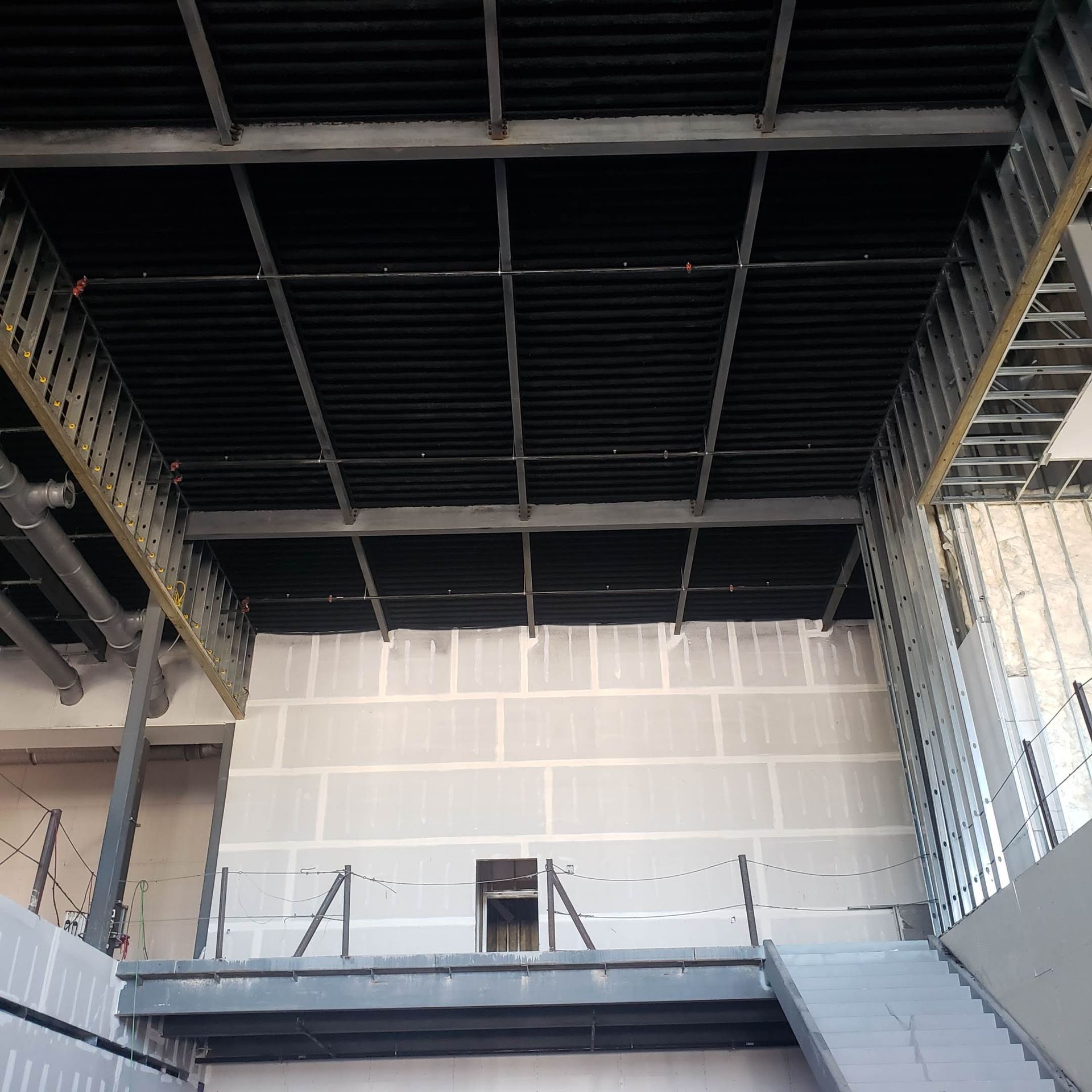 Interior view of a building under construction, featuring exposed steel beams, a dark ceiling, and light-colored block walls.