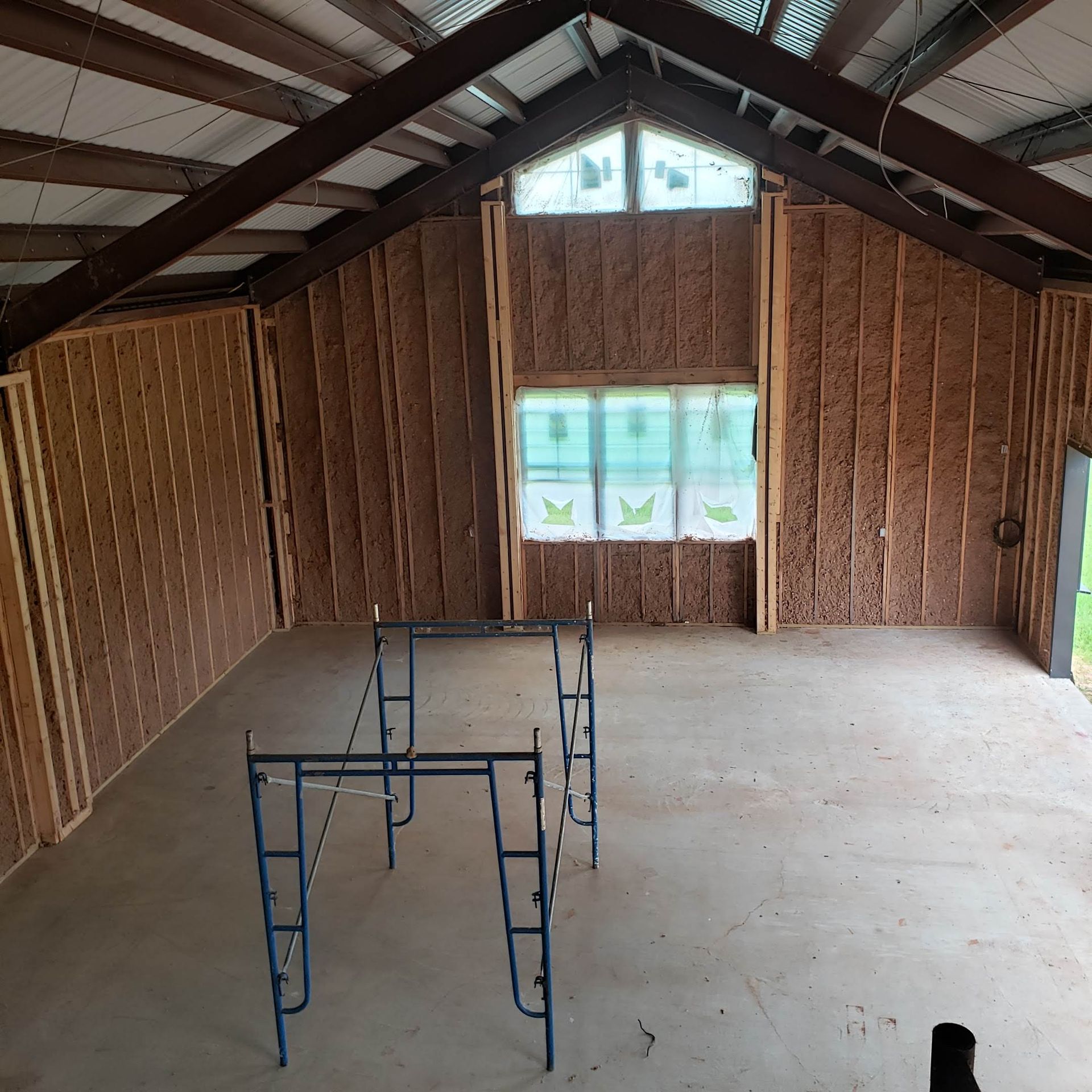 An interior view of a construction project featuring wood-framed walls with insulation and a metal roof structure.