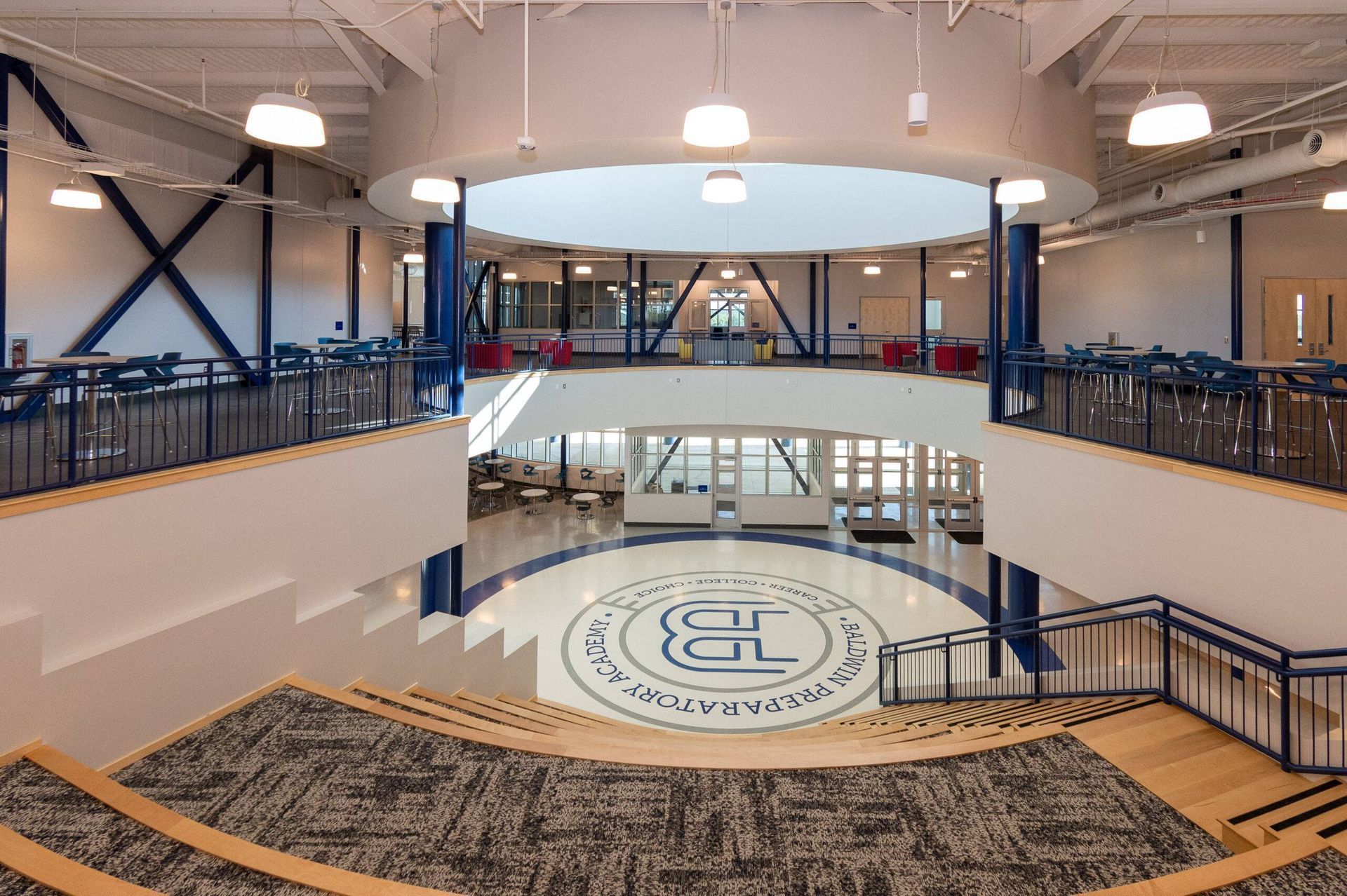 A multi-level interior space with tiered seating overlooking a ground floor circular lobby with a blue and white logo.