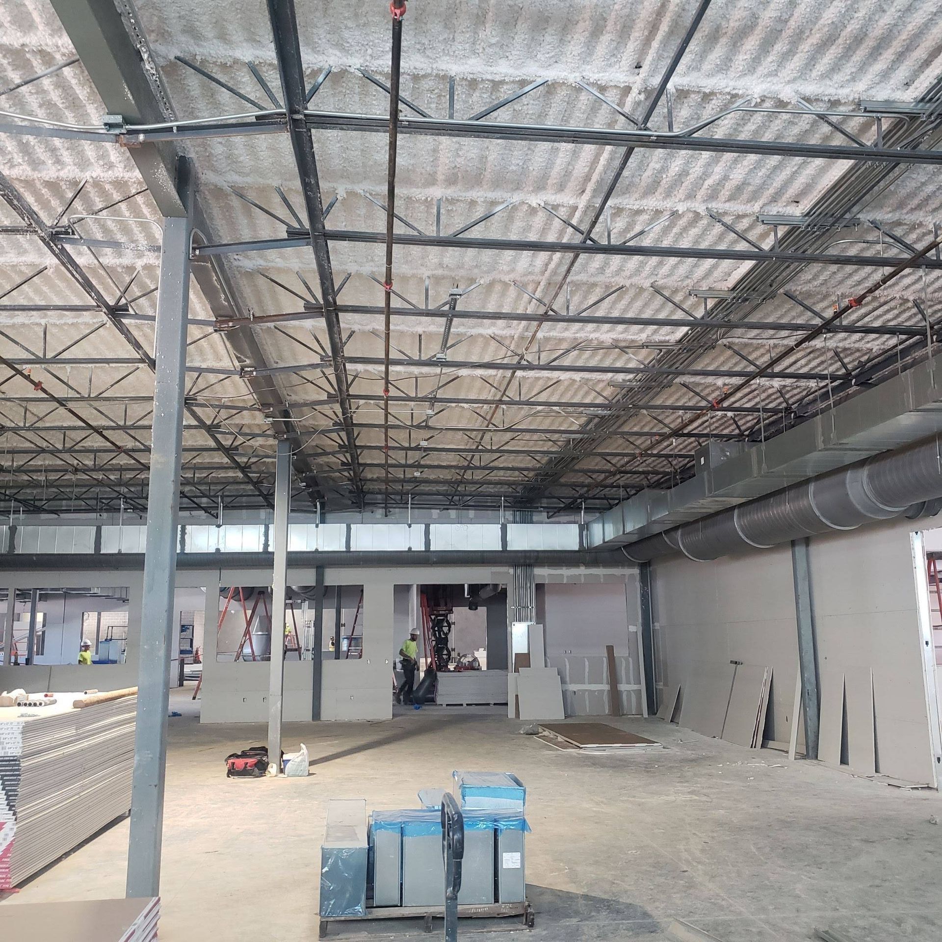 Interior of a construction site with exposed steel ceiling joists, white-sprayed decking, and grey metal wall framing.