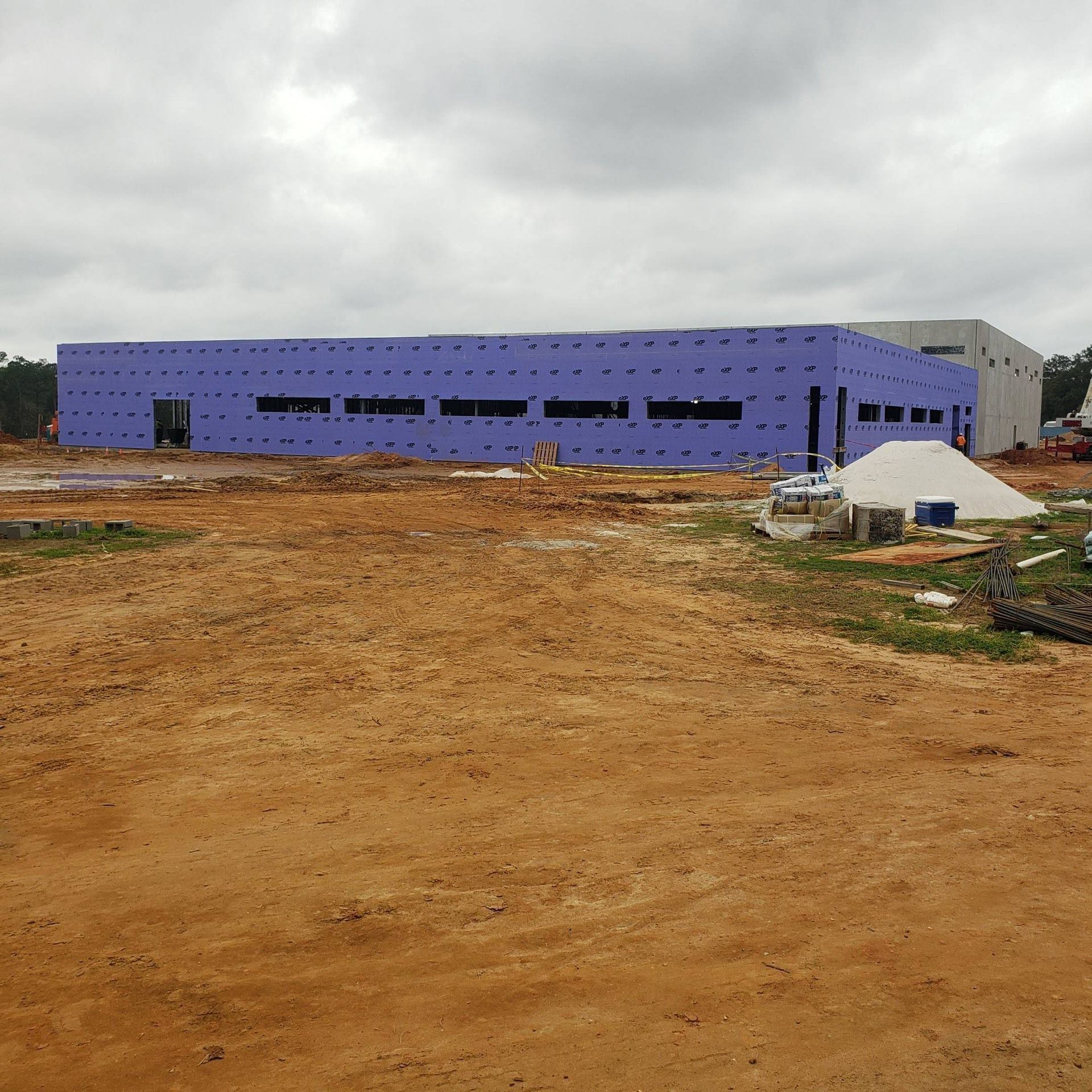 A long commercial building under construction with purple exterior sheathing, surrounded by a dirt construction site.