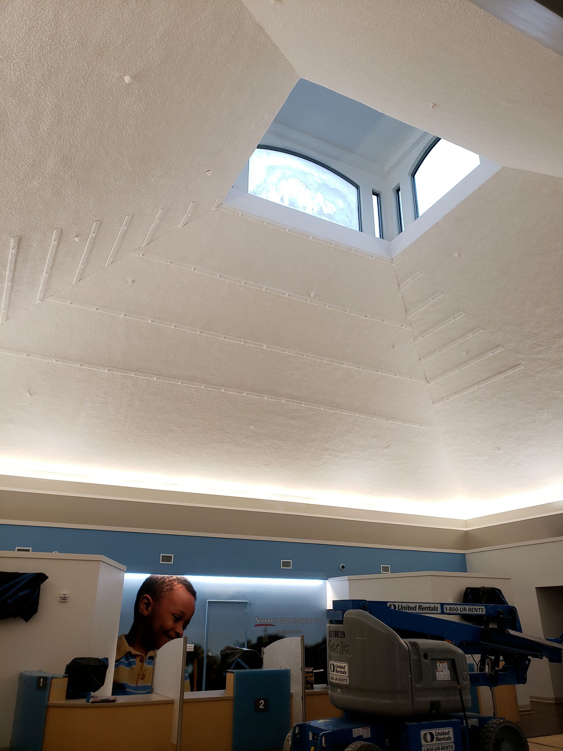 A worker at a construction site with a vaulted ceiling, a skylight, and cove lighting.