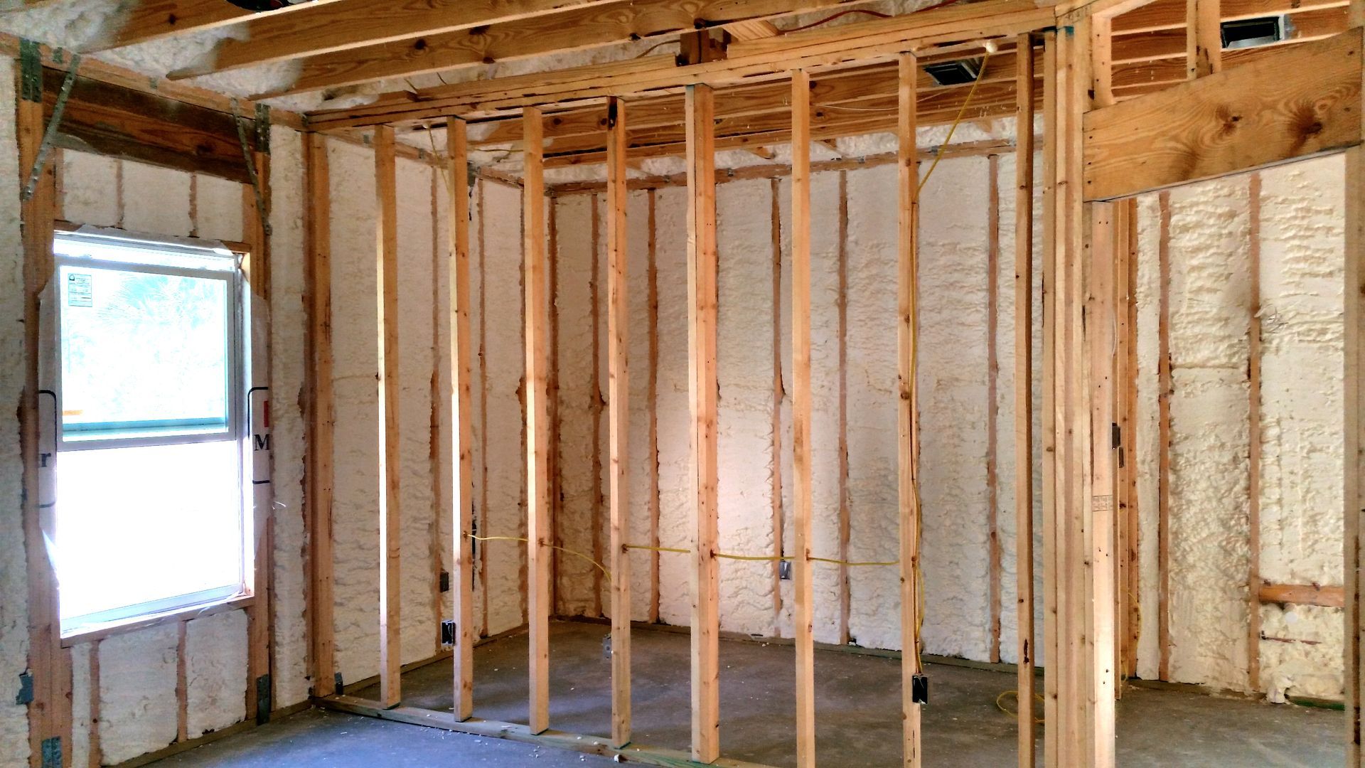 A room under construction with wooden wall framing and white spray foam insulation between the studs.