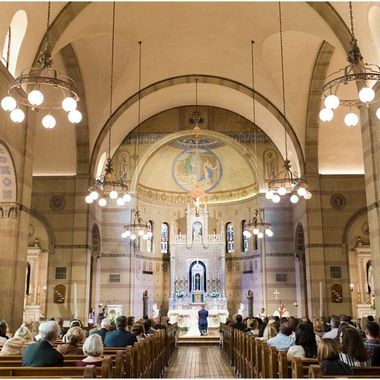 A bride and groom stand at the altar of a traditional, ornate church with high ceilings and rows of pews facing them.