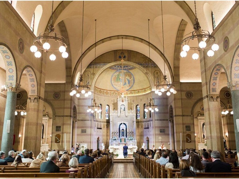 A congregation sits in pews inside a cathedral, facing an altar and a domed apse adorned with religious artwork.